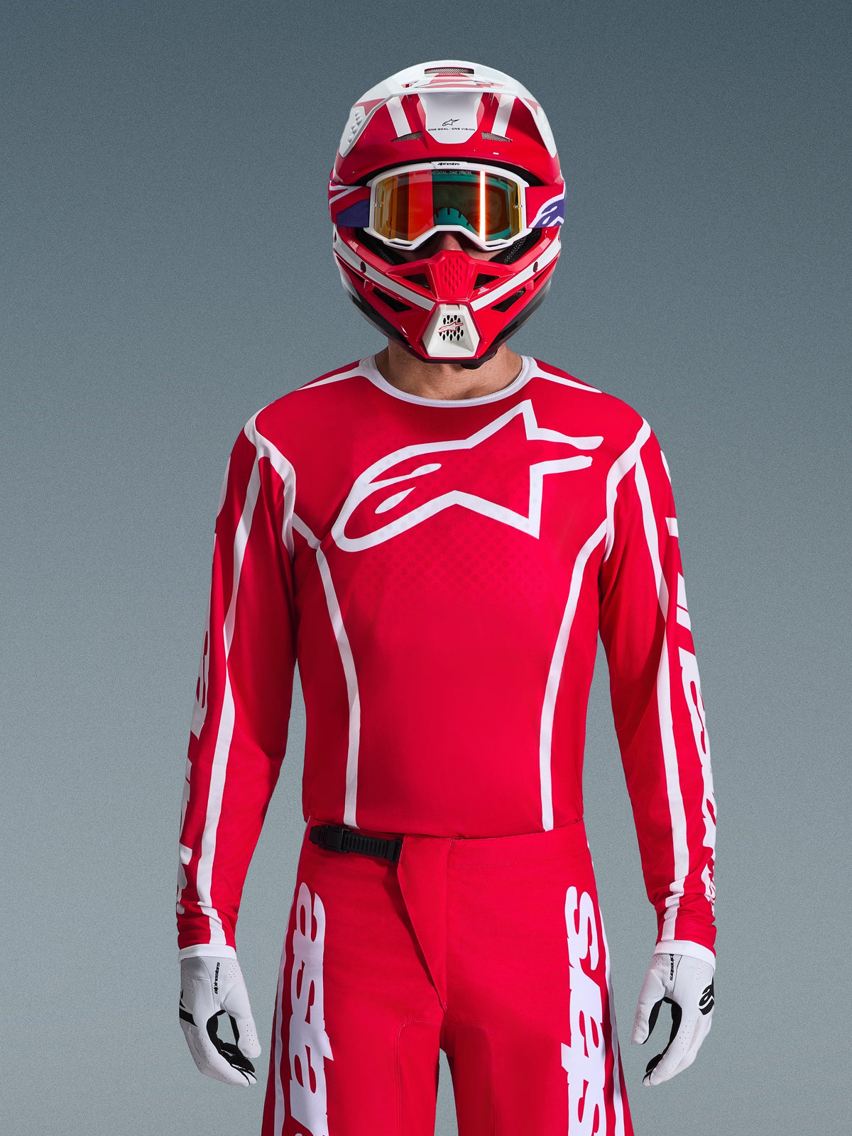 Alpinestars 2026 Fluid Apex Jersey, motorcross jersey, rood en wit, gedragen door een rijder met een bijpassende rood-witte helm en oranje crossbril, met een opvallend wit logo op de borst, sportieve pasvorm, onderdeel van een gecoördineerde off-road race-uitrusting