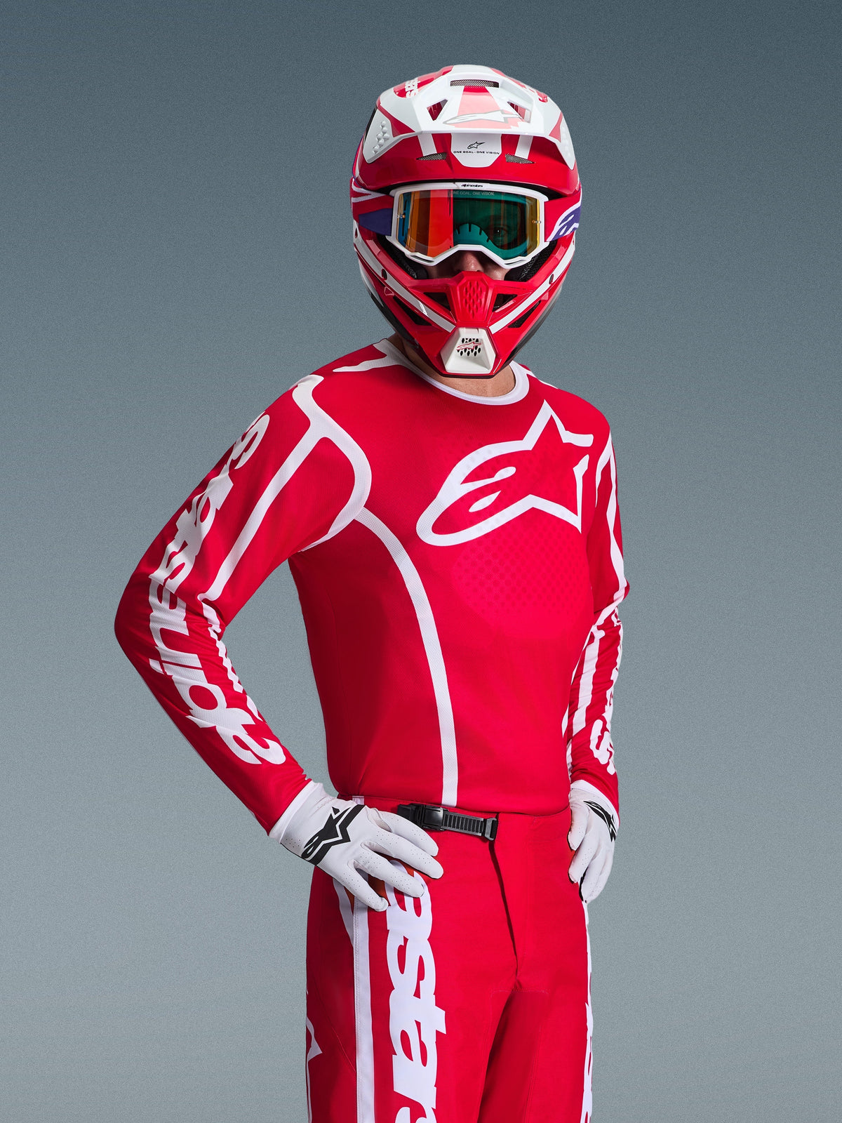 Alpinestars 2026 Fluid Apex uitrustingsset in rood en wit, motorcrosser met een rode jersey met witte logo's, bijpassende broek, witte handschoenen en een rood-witte helm met iriserende bril, gecoördineerde off-road race-outfit.