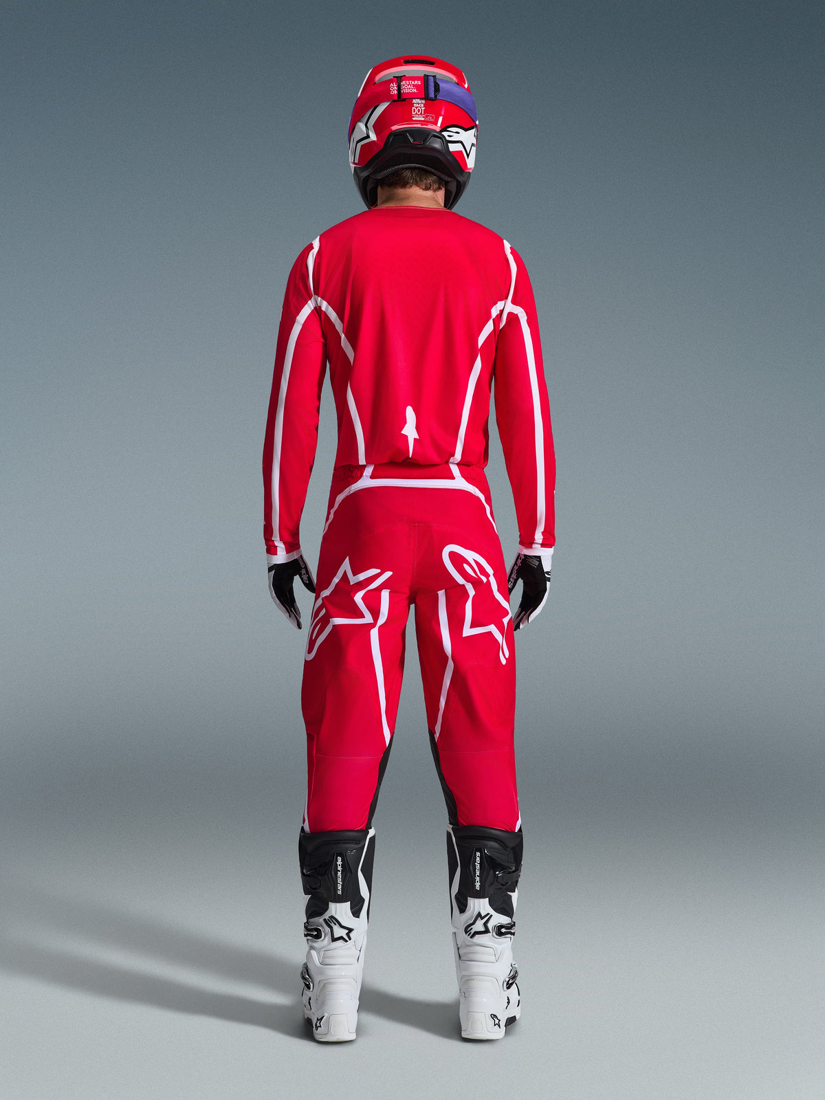 Achteraanzicht van een motorcrosser die de Alpinestars 2026 Fluid Apex Gear Set draagt, felrode jersey en broek met witte strepen en logo's, gecombineerd met wit-zwarte laarzen en een rode helm, professionele off-road race-uitrusting