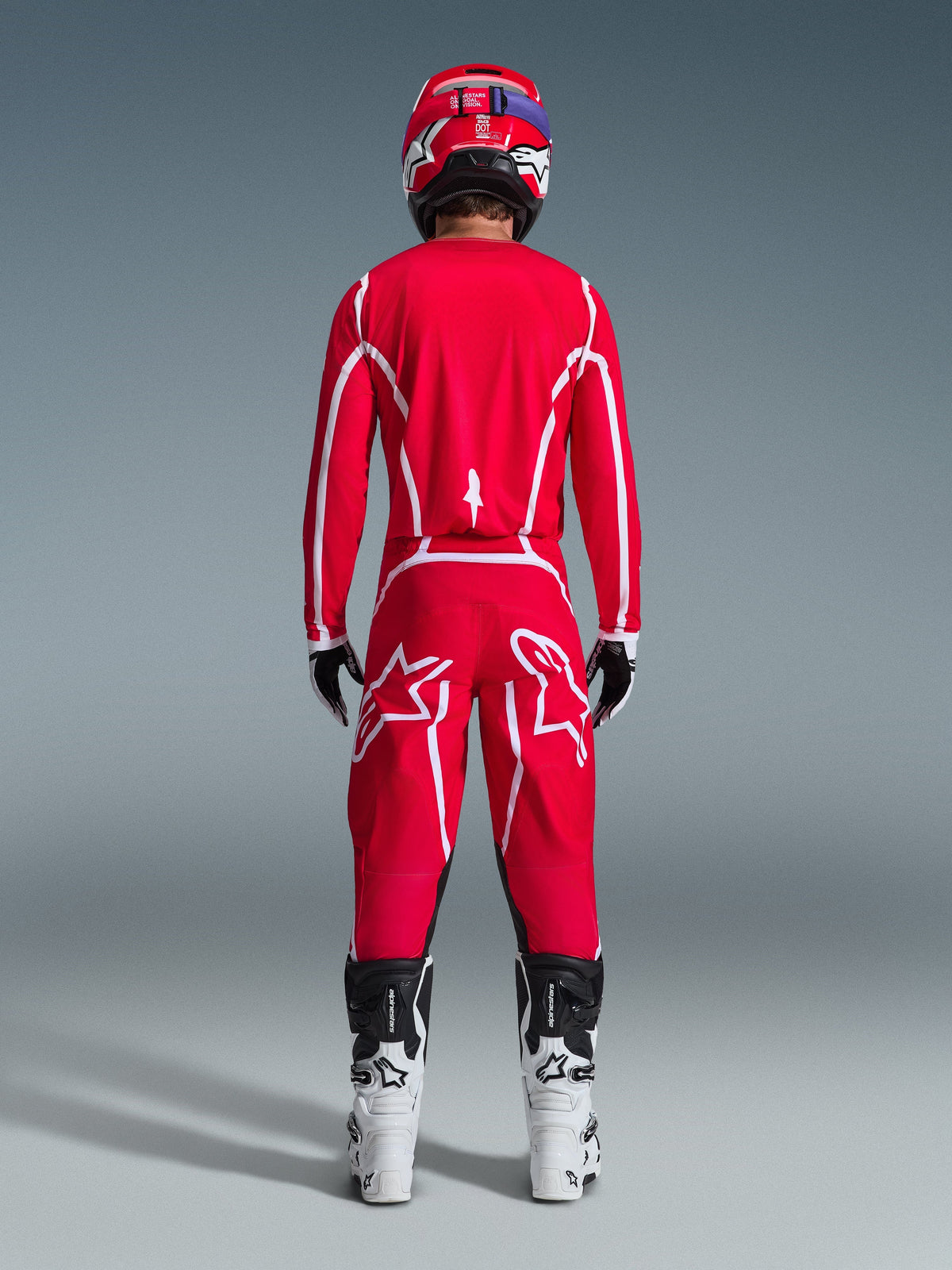 Motorcrosser van achteren gezien in de Alpinestars 2026 Fluid Apex Jersey in rood en wit, bijpassende rode broek met opvallende witte sterlogo's, een rode helm, wit-zwarte motorcrosslaarzen en zwart-witte handschoenen, complete uitrusting voor off-road racen