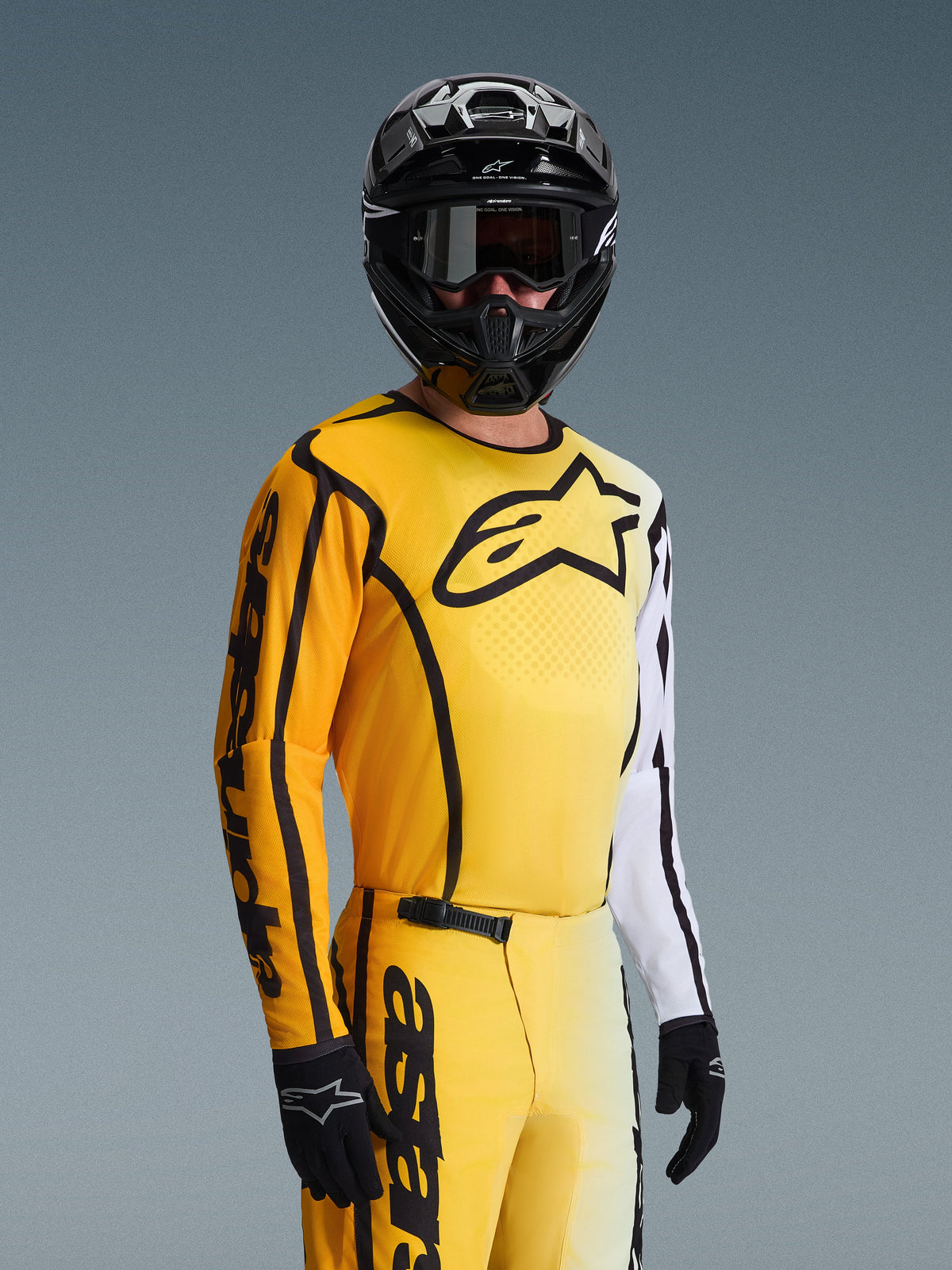 Alpinestars 2026 Fluid Apex Jersey, motocross shirt, geel en zwart met witte accenten, gedragen door een rijder met een zwarte helm en bril, groot zwart sterlogo op de borst, bijpassende off-road race-uitrusting