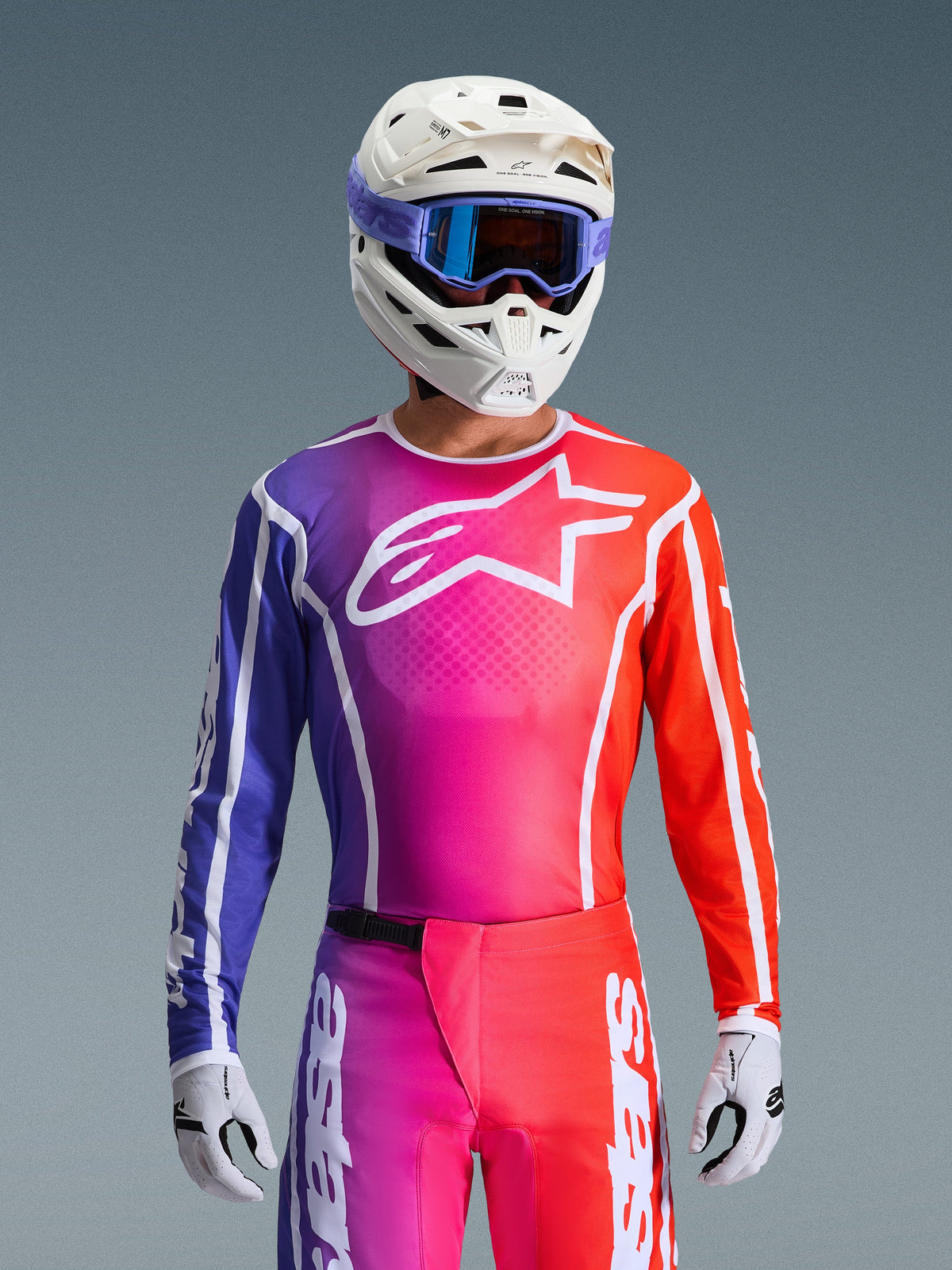 Alpinestars 2026 Fluid Apex Gear Set, motorcross jersey en broek met een paars, roze en oranje kleurverloop, wit Alpinestars-sterlogo op de borst, witte helm en paarse crossbril, hoogwaardige atletische pasvorm voor off-road rijden
