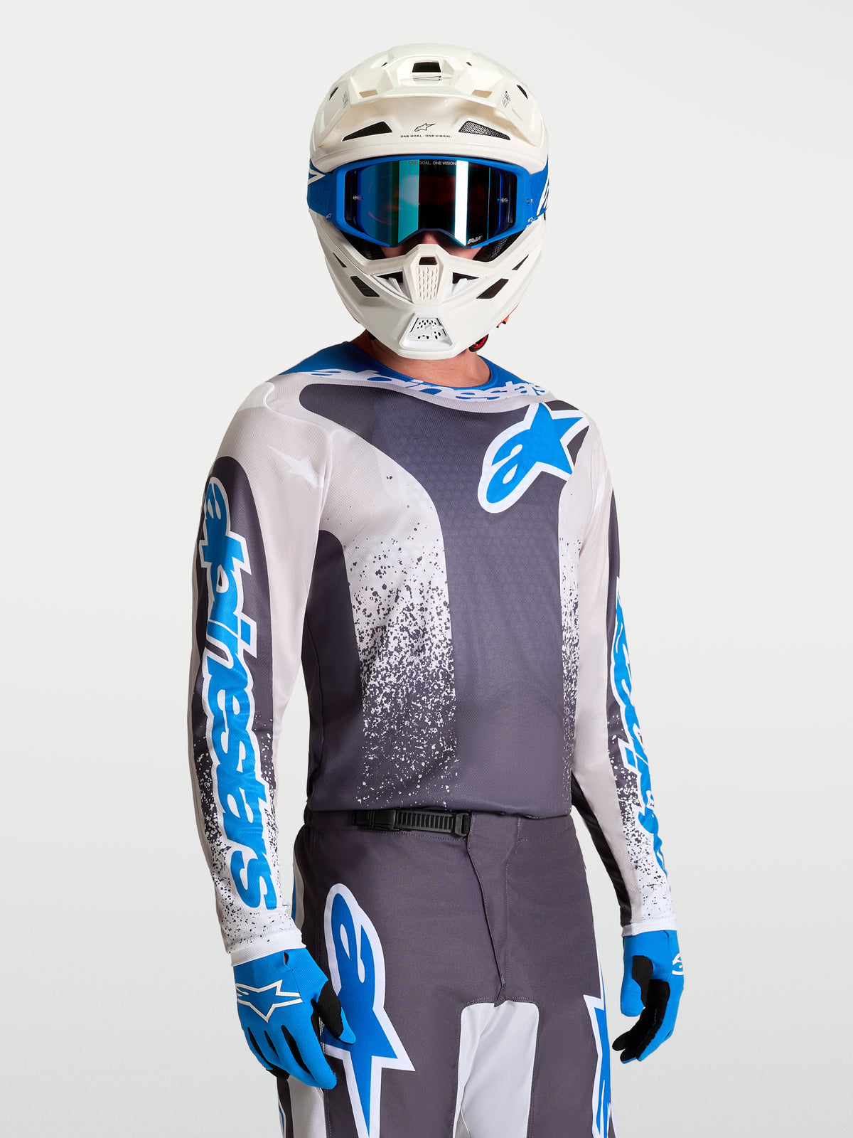 Alpinestars Fluid Drag Jersey, grijze en blauwe motocross jersey voor heren met witte helm en blauwe handschoenen.