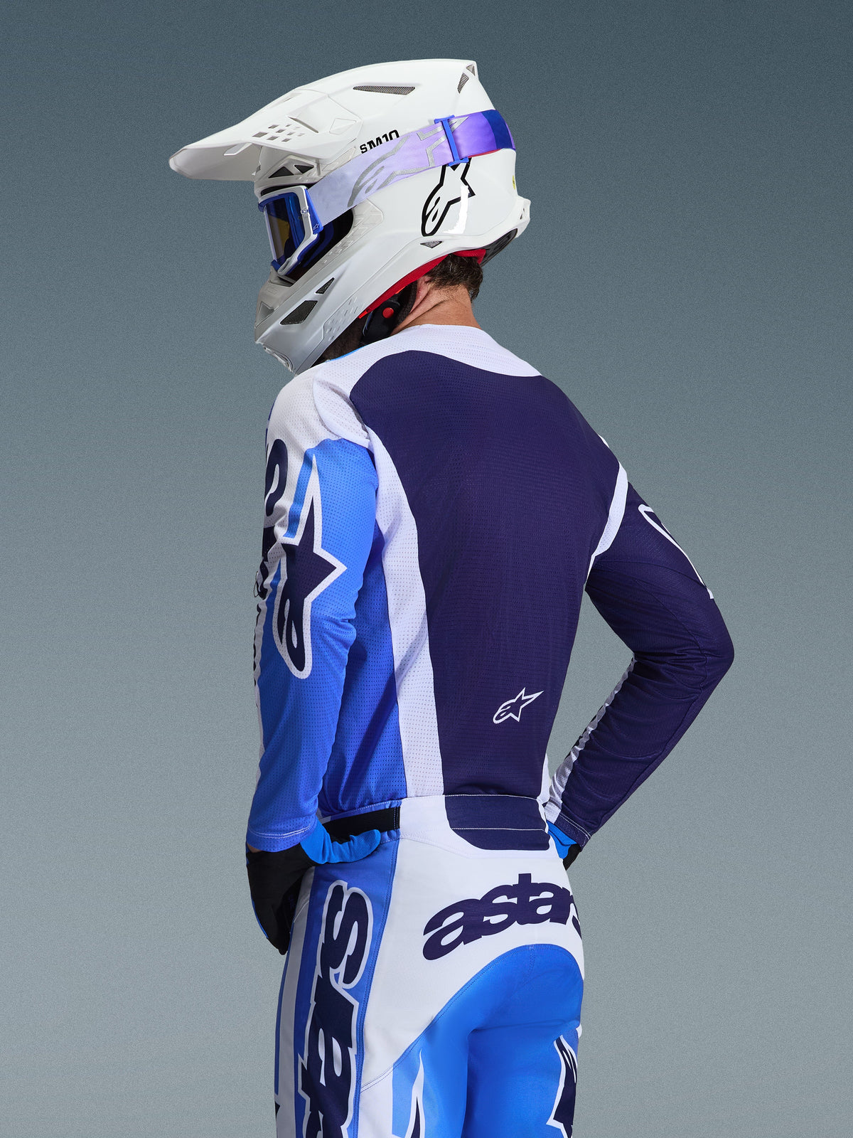 Motocrossrijder die de Alpinestars 2026 Racer Air Portl Jersey draagt in Ucla Blue en wit, achteraanzicht met de nadruk op het ademende marineblauwe mesh rugpaneel, gedragen met bijpassende broek en een witte Alpinestars-helm met blauwe bril, gecoördineerde motorcrossuitrusting.