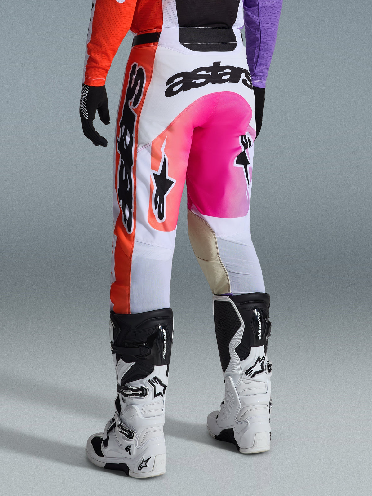 Alpinestars 2026 Racer Air Portl broek, motorcross broek, meerkleurig met wit, felroze en oranje, achteraanzicht gedragen met witte en zwarte Alpinestars laarzen, voorzien van opvallende branding en duurzame raceconstructie