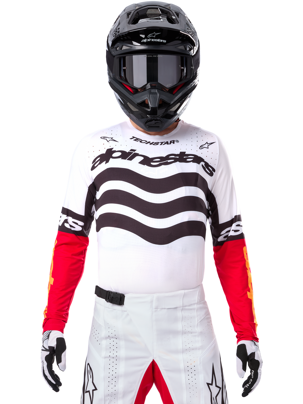 Motorcrossrijder in volledige race-uitrusting, Limited Edition Techstar Deep Jersey in wit en zwart met rode mouwen, voorzien van golvende graphics en opvallende Alpinestars-branding, witte motorcrossbroek, zwarte helm en motorcrossbril, gecoördineerde outfit voor off-road racing.