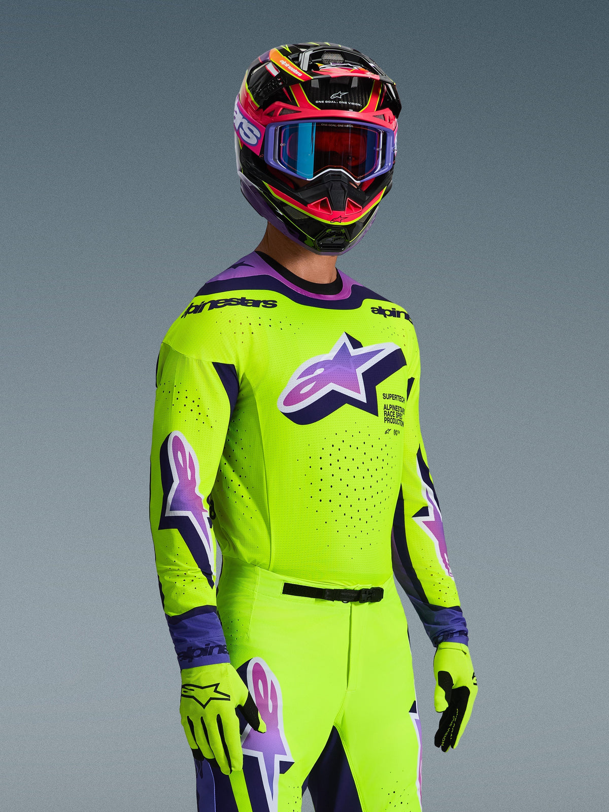 Motocrossrijder in de Alpinestars 2026 Supertech Vista Jersey, felgeel met paarse en zwarte accenten, bijpassende gele broek en handschoenen, meerkleurige helm met paarse crossbril, voorzien van lasergesneden perforaties en een groot Astar-logo op de borst, gecoördineerde professionele race-outfit