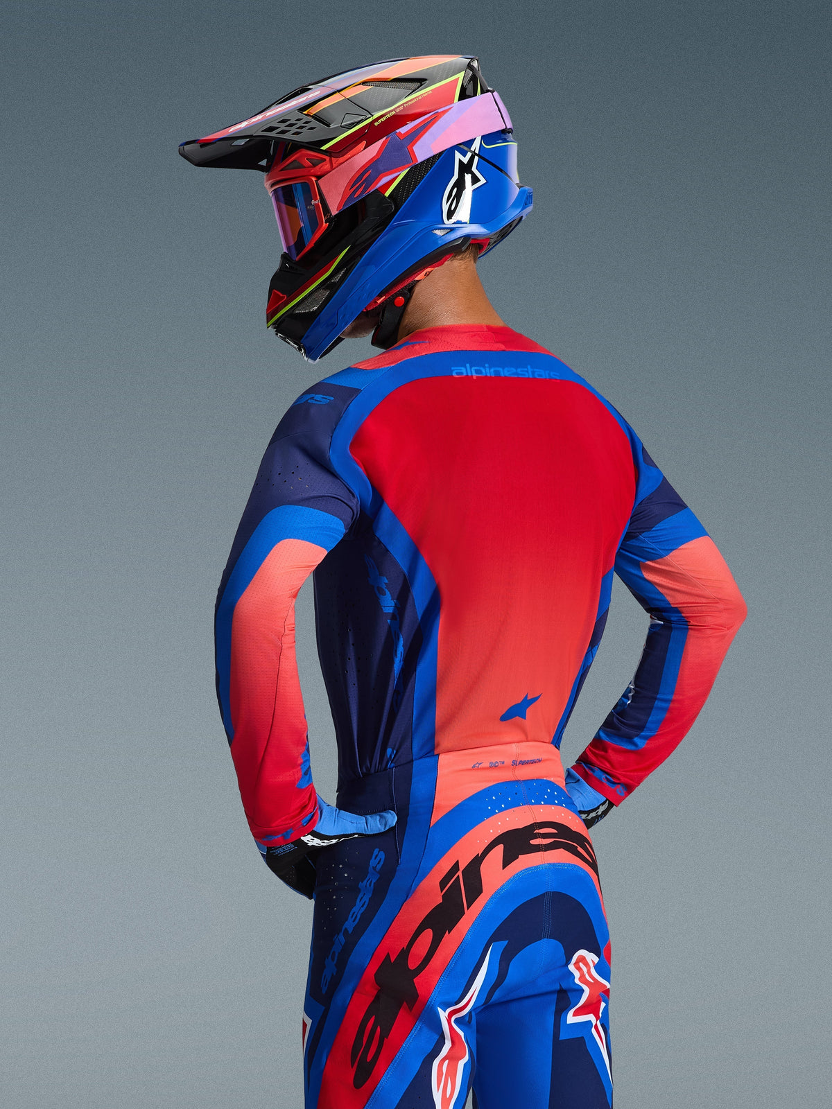 Alpinestars 2026 Supertech Vista Gear Set, Motocross Jersey and Pants in Dark Navy, Hot Coral, and Cobalt, rear view of a rider wearing a matching multicolored helmet and goggles, athletic race-fit racing apparel