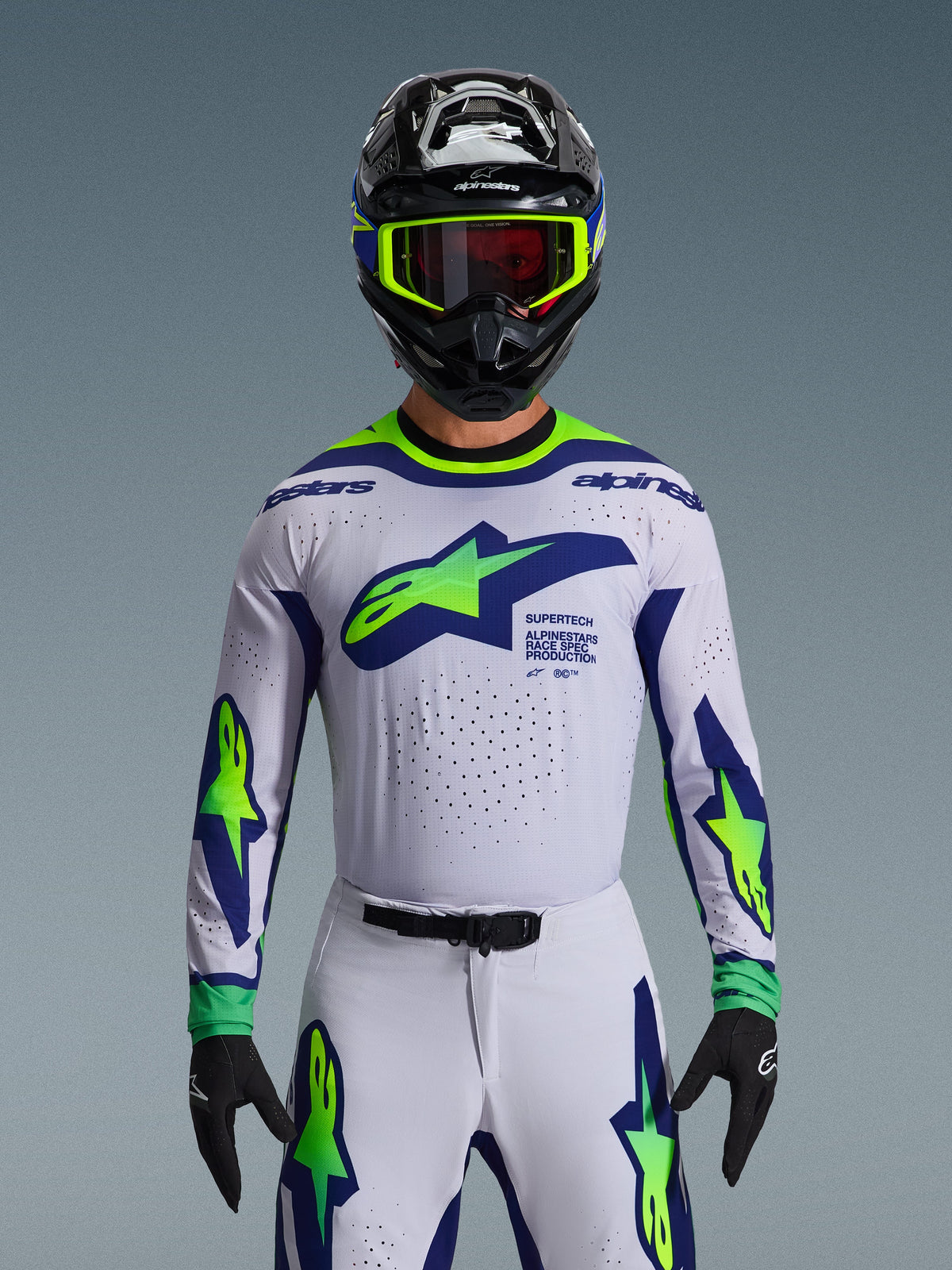 Alpinestars 2026 Supertech Vista Jersey, motocross jersey, lichtgrijs, fluo geel en blauw, gedragen door een rijder met bijpassende broek en zwarte helm, voorzien van een groot logo op de borst en lasergesneden perforaties voor ventilatie, atletische pro-level pasvorm