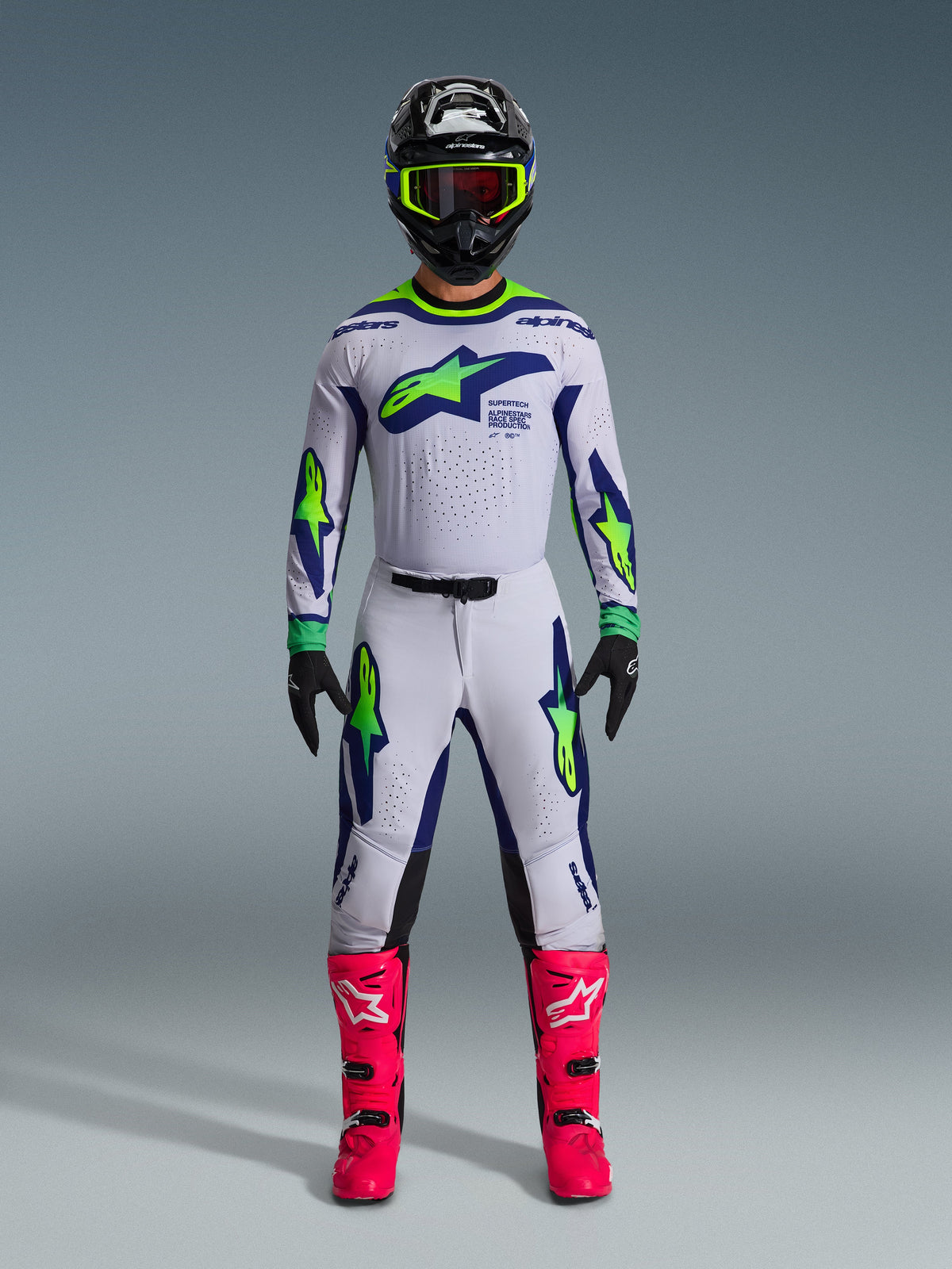 Motocrossrijder in de 2026 Supertech Vista Jersey in Light Gray Yellow Fluo Blue, compleet met bijpassende broek, felroze laarzen en een zwarte helm met neon accenten, pro-level off-road race-uitrusting.