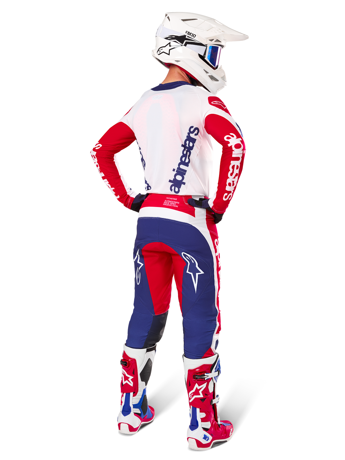 Motorcrosser van achteren gezien in de Alpinestars Limited Edition Techstar Fortitude Jersey en uitrustingsset, Bright Red White Blue kleurstelling, met witte Alpinestars-branding op de rode mouwen en een navy logo op de witte achterkant, gecombineerd met een witte motorcrosshelm en bijpassende racelaarzen.