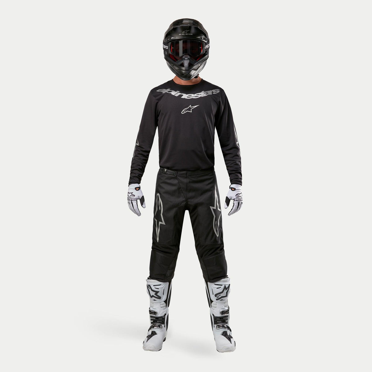 Motorcrossrijder in complete race-uitrusting, Alpinestars 2024 Fluid Graphite Jersey in Black Silver, zwarte broek met zilveren sterlogo's, zwarte helm met rode crossbril, wit-zwarte laarzen en handschoenen, gecoördineerde motorcross outfit