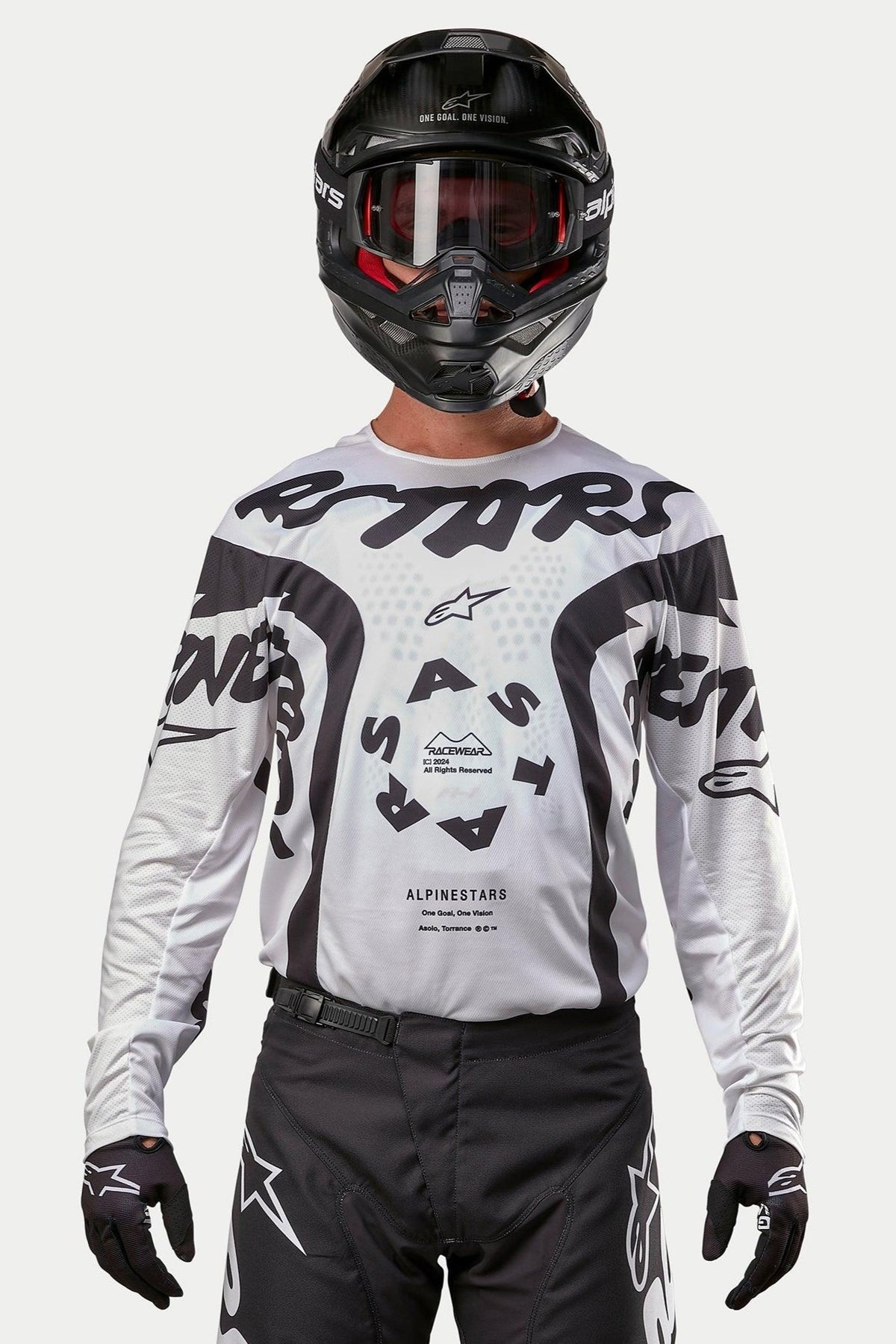 Motocross rider wearing the Alpinestars 2024 Racer Hana Jersey in White and Black, paired with a black helmet and black motocross pants, featuring bold black 'ASTARS' graphics and a circular central logo, professional off-road racing gear