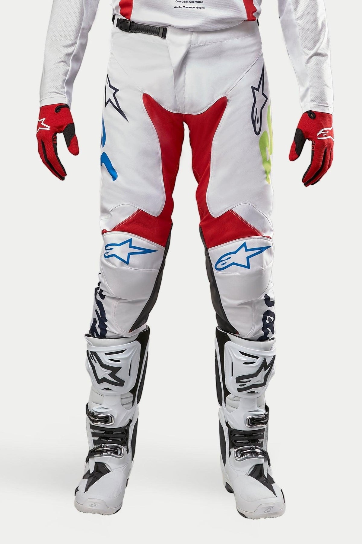 Alpinestars 2024 Racer Hana crossbroek, motorcrossbroek, wit meerkleurig met rode, blauwe en limoengroene accenten, gedragen met witte en zwarte laarzen en rode handschoenen, voorzien van Alpinestars-logo's op de knieën en een duurzaam technisch ontwerp voor off-road racen