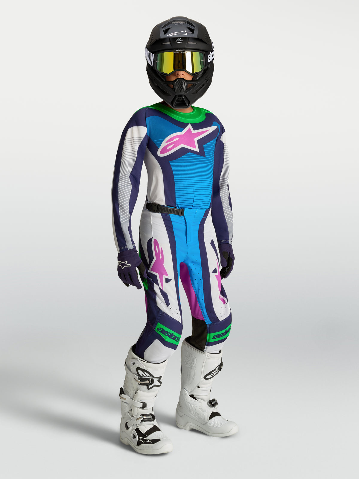 Alpinestars Jeugd Supertech Maven Gear Set, wit en blauw motocrossjersey en broek met groene accenten, zwarte helm en witte laarzen.