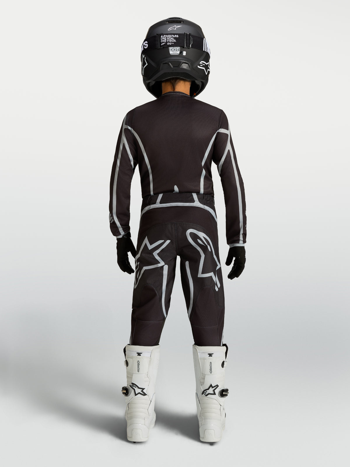 Alpinestars Jeugd Fluid Apex V2 jersey en motocrossuitrusting, zwart en zilver, achteraanzicht met witte motorlaarzen.
