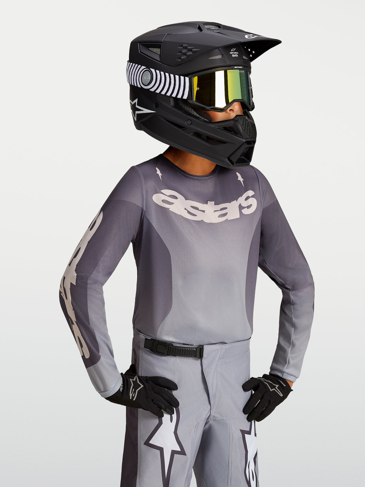 Alpinestars Jeugd Fluid Amber Jersey 2027, motocrossjersey in zand en grijs, gedragen met een zwarte helm en crossbril.