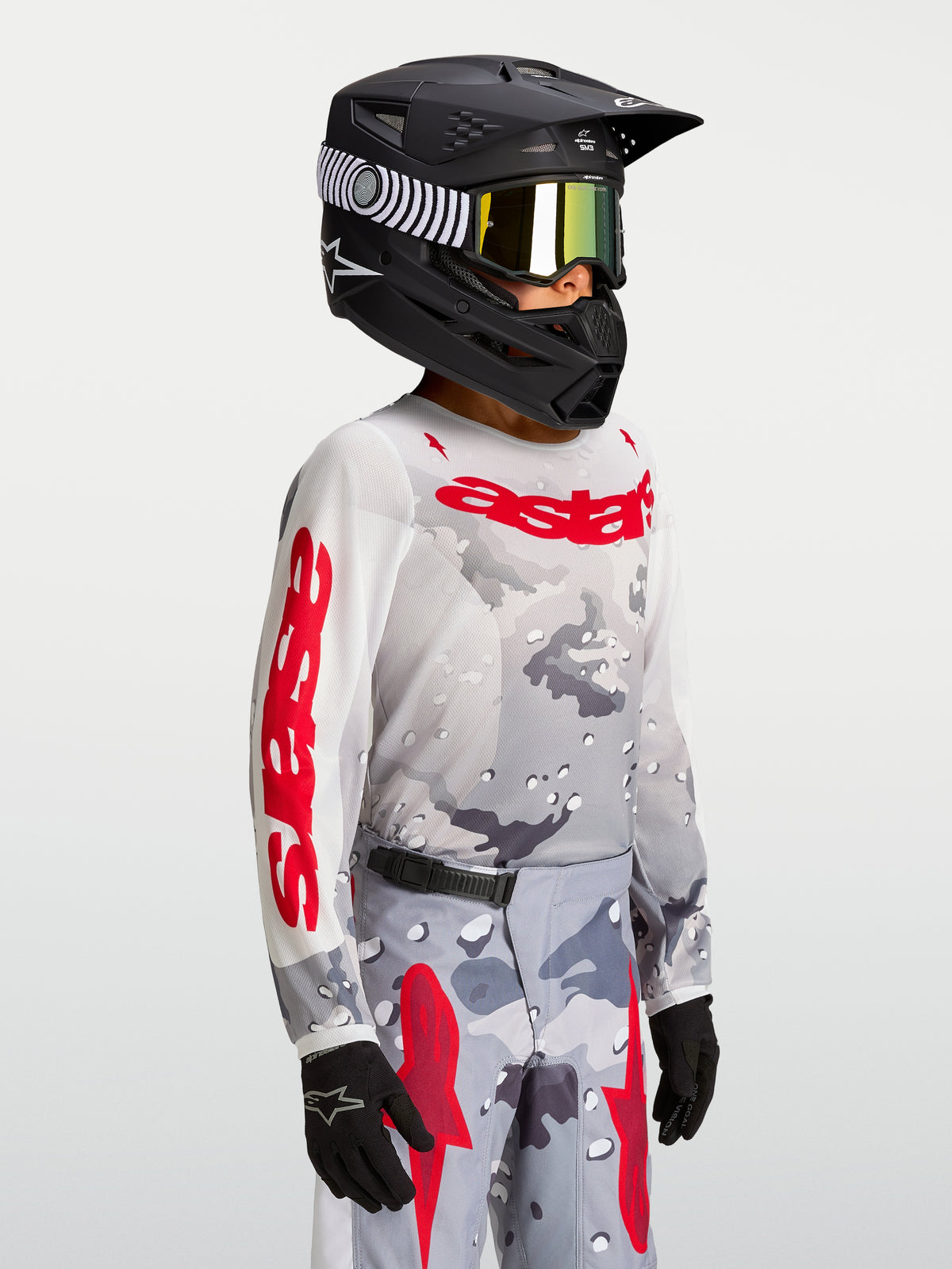 Alpinestars Jeugd Fluid Lone Jersey 2027, motocrossjersey in grijs camo en rood, gedragen door model met helm.