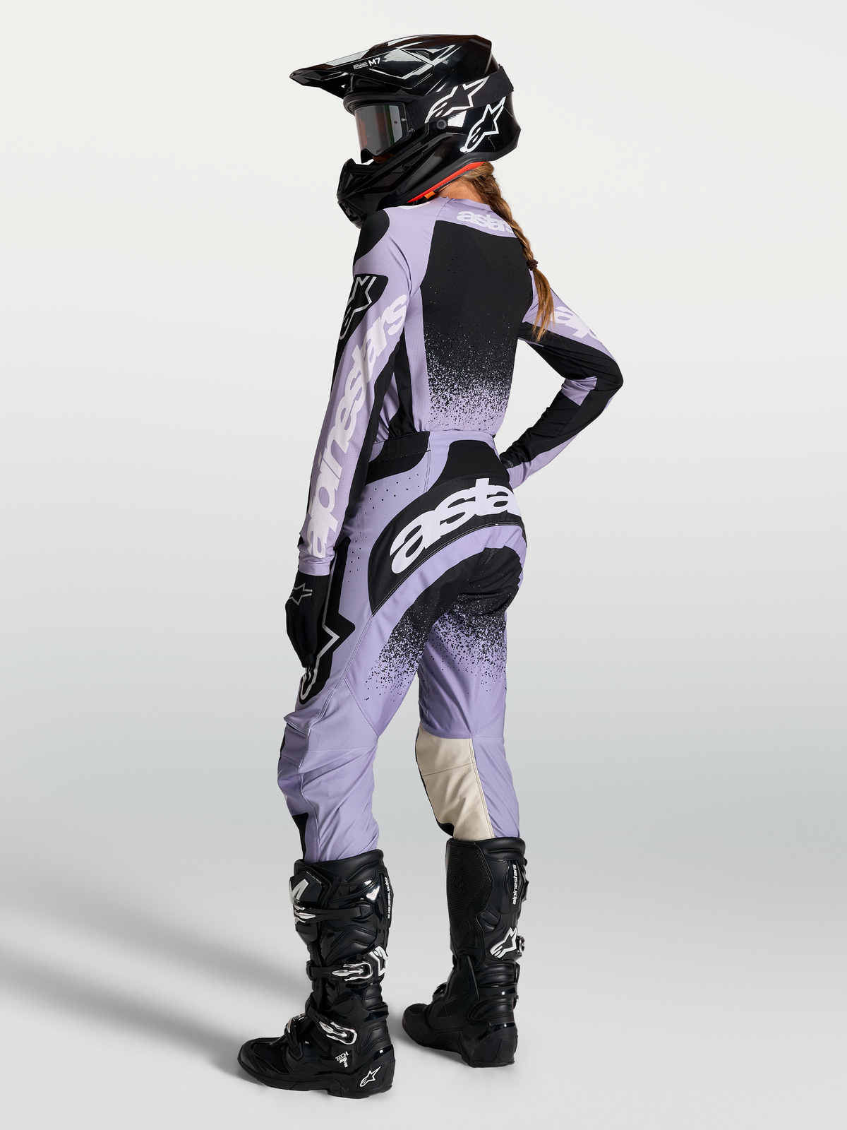 Alpinestars Stella Techstar Swan broek, dames-motorcrossbroek voor off-road racing, lichtpaars en zwart, ergonomische racepasvorm, gedragen door een model met bijpassende jersey en zwarte motorlaarzen.
