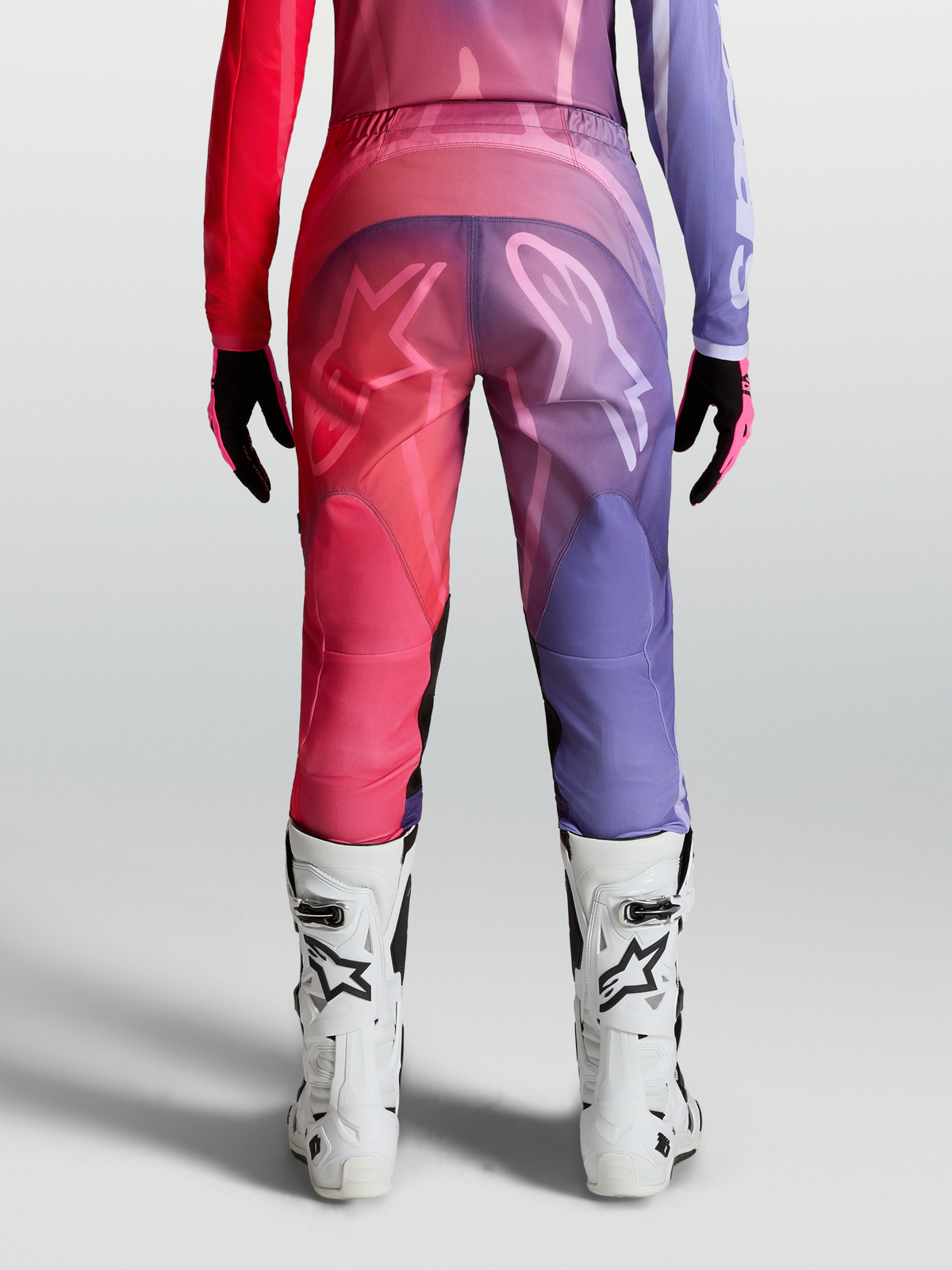 Alpinestars Stella Fluid Kepler Broek, paarse en roodroze dames motorcrossbroek met ergonomische pasvorm en witte MX-laarzen.