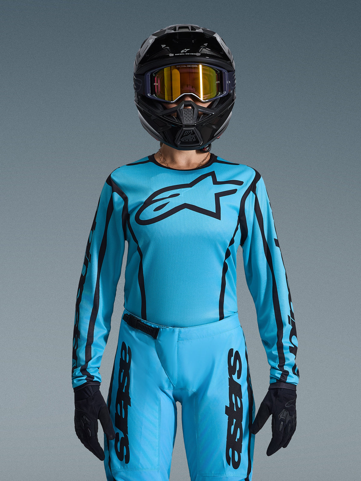 Motocrossrijder in Alpinestars Stella Fluid Apex Gear Set 2026 voor dames, lichtblauwe jersey met zwarte omlijningen en logo, bijpassende broek, zwarte helm met iriserende gouden crossbril en zwarte handschoenen, gecoördineerde dames motocross race-outfit