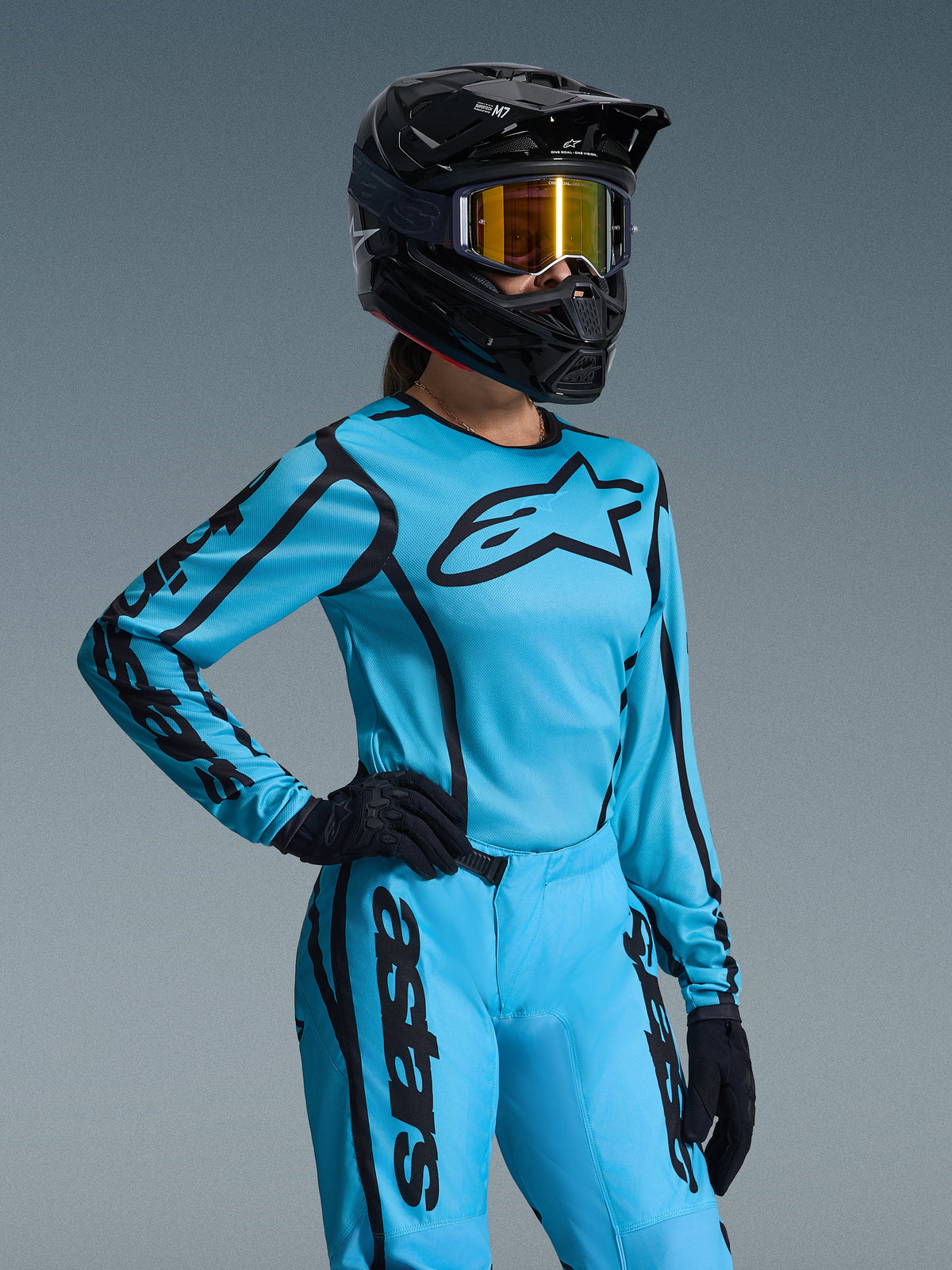 Alpinestars 2026 Stella Fluid Apex gearset voor dames, felblauw en zwart, motorcross jersey en broek met zwarte logo's, gedragen met een zwarte helm, goudkleurige spiegelbril en zwarte handschoenen, specifieke damespasvorm voor off-road racen