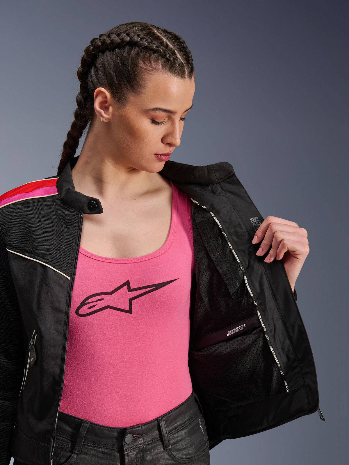 Vrouwelijke motorrijder draagt de Alpinestars Stella T-Dyno Air Jas in Black Bright Red Fuchsia, gedeeltelijk open om het waterdichte binnenvak te tonen, gedragen over een roze tanktop met logo, met nadruk op de ademende mesh-panelen en de getailleerde biker-pasvorm.