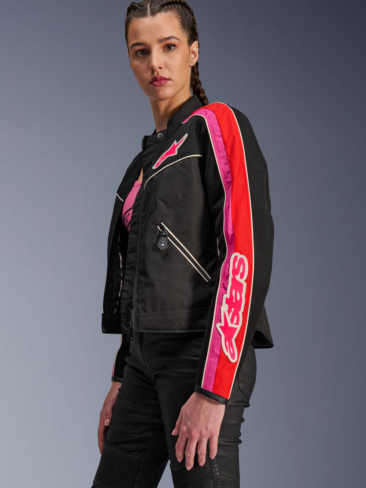Alpinestars Stella T-Dyno Air damesjas, motorjas voor dames, zwart met felrode en fuchsia accenten, gedragen met een zwarte broek, voorzien van een roze Astars-logo op de borst en mouw, getailleerde bikerpasvorm met mesh-panelen voor ventilatie.