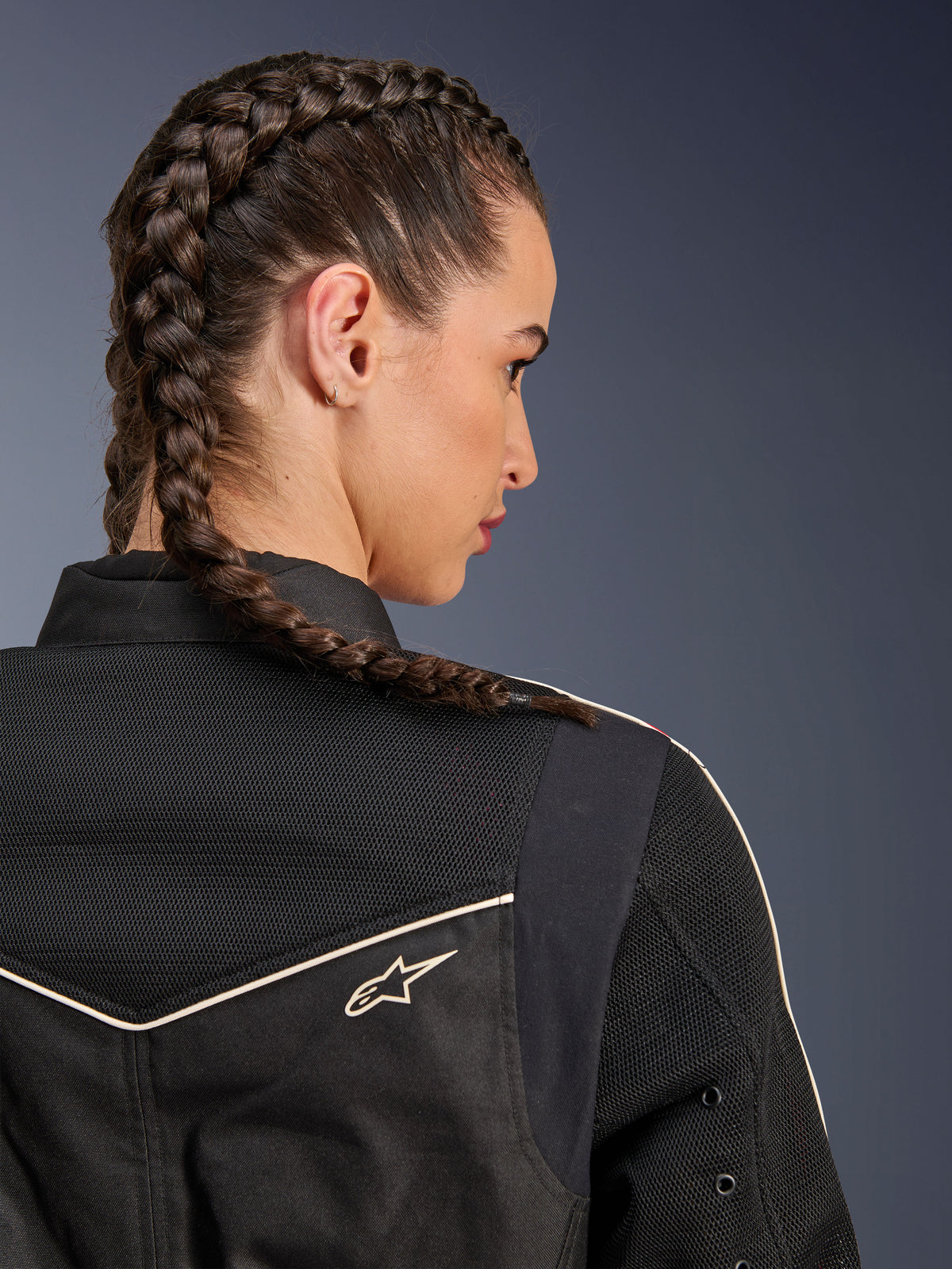 Vrouw die de Alpinestars Stella T-Dyno Air jas draagt, close-up achteraanzicht gericht op de schouders en het juk, zwart met ademende 3D mesh-panelen, witte biezen en klein Astars-logo, model met gevlochten haar, urban motorkleding