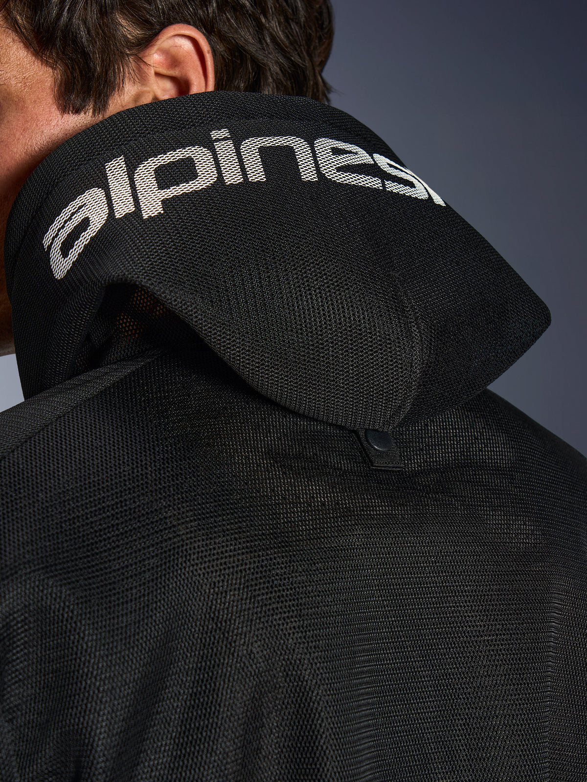 Alpinestars Chrome Superairflow Hoodie, zwart, detailweergave van de 3D-mesh capuchon met witte Alpinestars-branding over de bovenkant, inclusief de stabilisatiedrukknoop aan de achterzijde, geventileerde textiele motorkleding voor extreme hitte