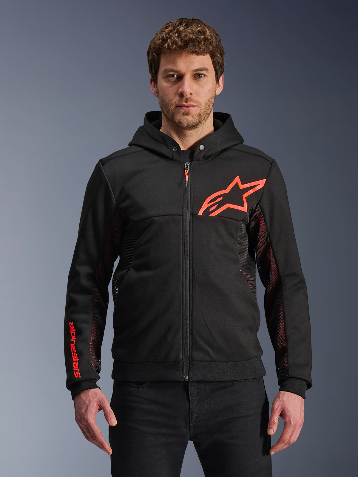 Alpinestars Chrome Air Sport Hoodie, zwarte hoodie met rits met fluo rood sterlogo en accenten op de mouwen, rode mesh zijpanelen voor ventilatie, casual stedelijke motorkleding gedragen door een model