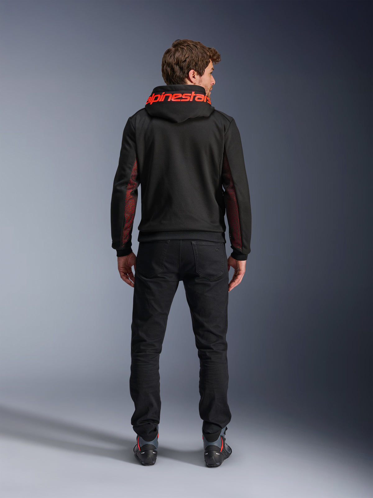 Alpinestars Chrome Air Sport Hoodie, casual motorjas, zwart en fluorood, achteraanzicht van een man die de hoodie draagt, met rode Alpinestars-branding op de capuchon en rode mesh-panelen op de mouwen, gecombineerd met een zwarte broek.