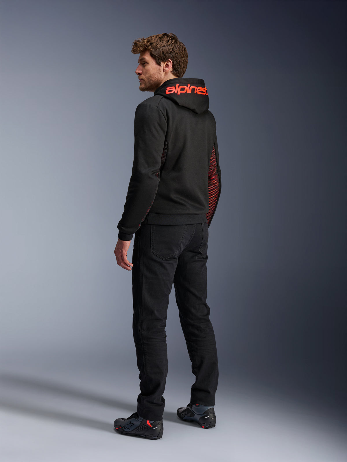 Alpinestars Chrome Air Sport Hoodie, urban motorhoodie, zwart en fluo rood, achteraanzicht met rode Alpinestars-branding op de capuchon en mesh zijpanelen, gedragen met zwarte motorbroek en technisch schoeisel