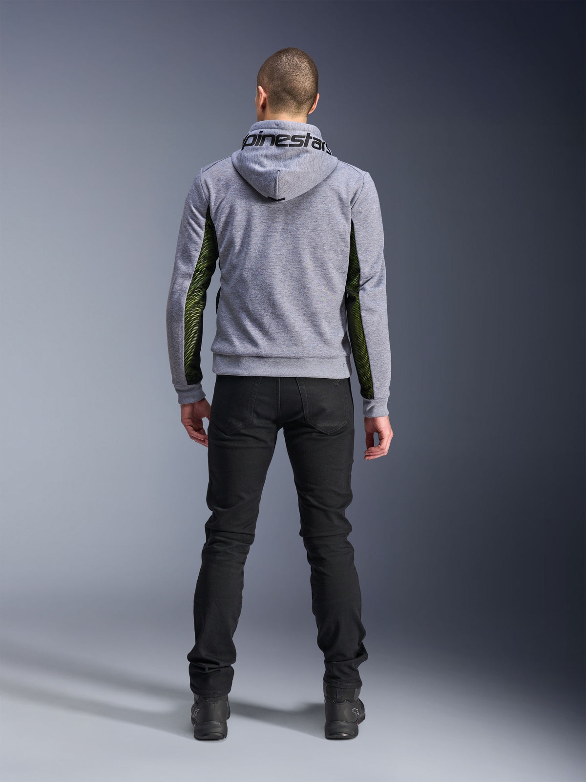 Alpinestars Chrome Air Sport Hoodie, Gray Heather Black, achteraanzicht van een motorhoodie met groene high-flow mesh panelen aan de zijkanten en mouwen, tech fleece-constructie met Alpinestars-branding op de capuchon, gedragen met een zwarte broek