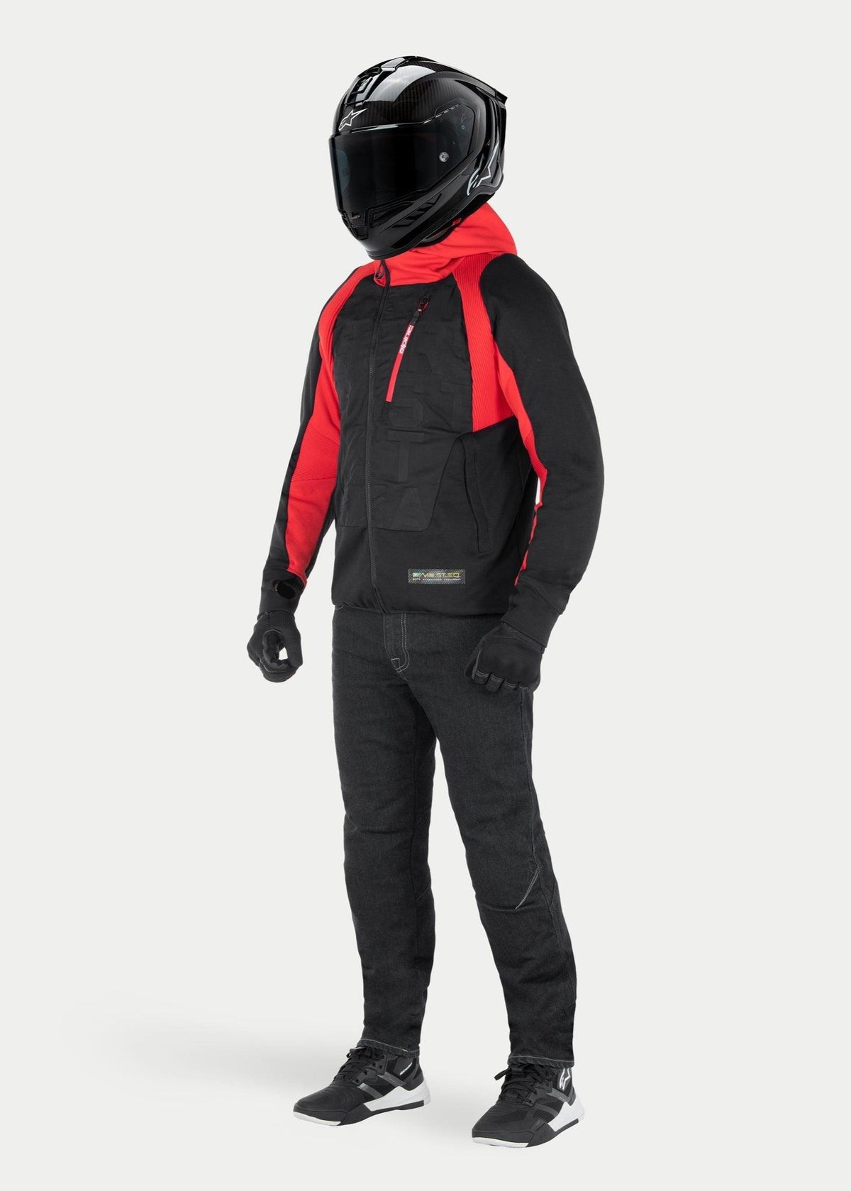 Alpinestars MO.ST.EQ Hybrid jas met capuchon in Black Flame Red, urban motorhoodie met rode capuchon en schouderaccenten, gedragen met een zwarte integraalhelm en motorbroek, eigentijds op streetwear geïnspireerd ontwerp