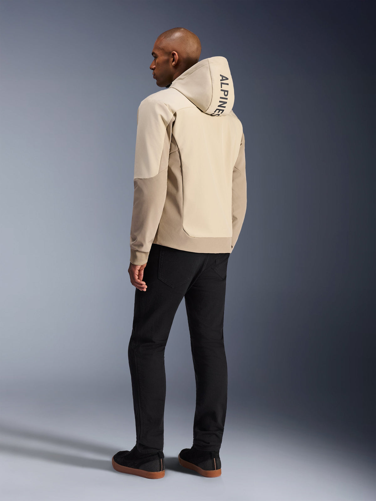 Alpinestars Radium Tech Hoodie in Mastic Aluminum, stedelijke motorjas, achteraanzicht op model met de capuchon omhoog, verticale ALPINESTARS-branding op de capuchon, gecombineerd met een zwarte broek, moderne textielconstructie voor bescherming tijdens stedelijk rijden