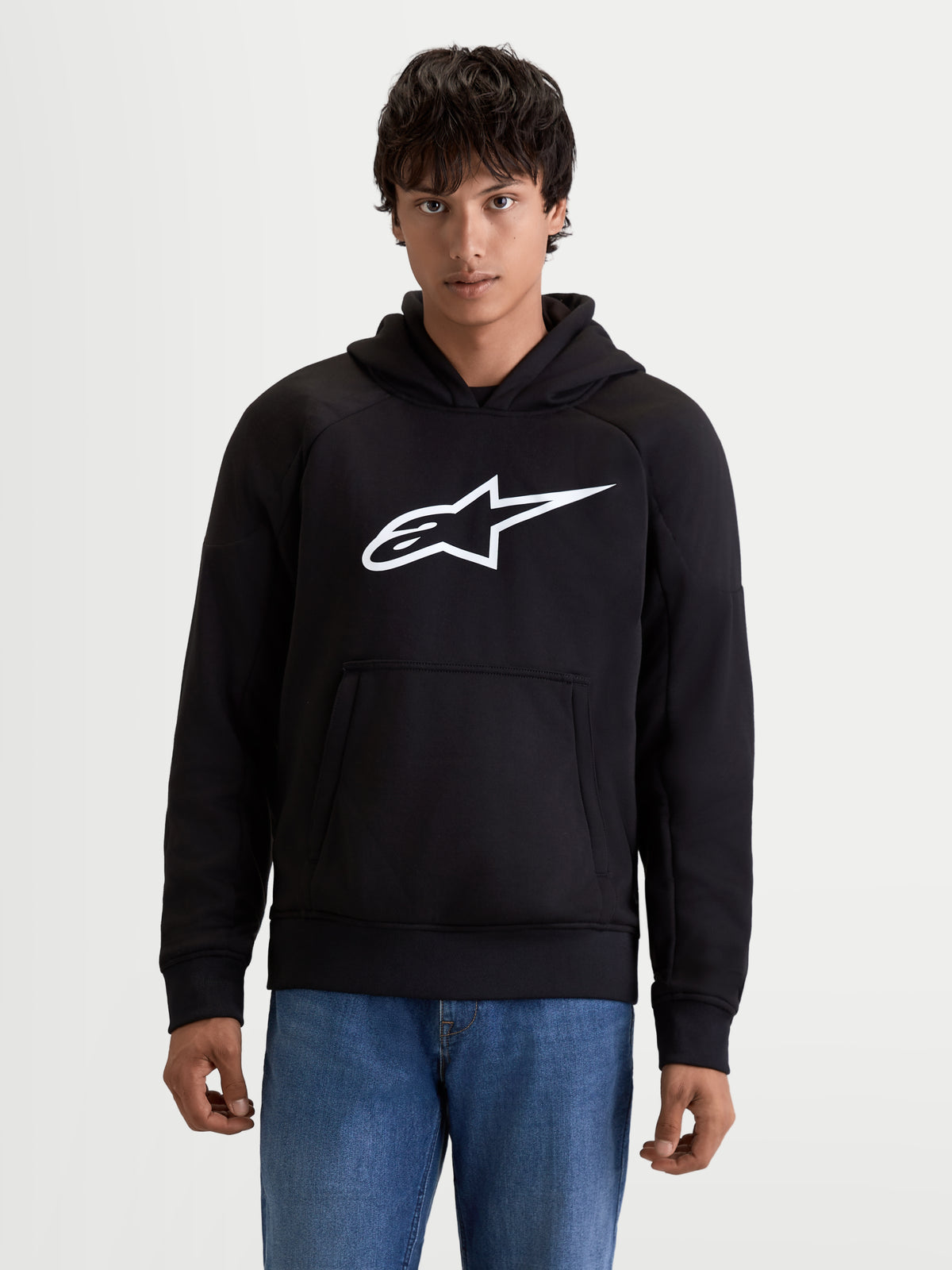 Alpinestars Ageless Hoodie, urban motorhoodie voor heren in zwart met wit logo op de borst, kangoeroezak aan de voorkant en casual textielconstructie, vooraanzicht op model
