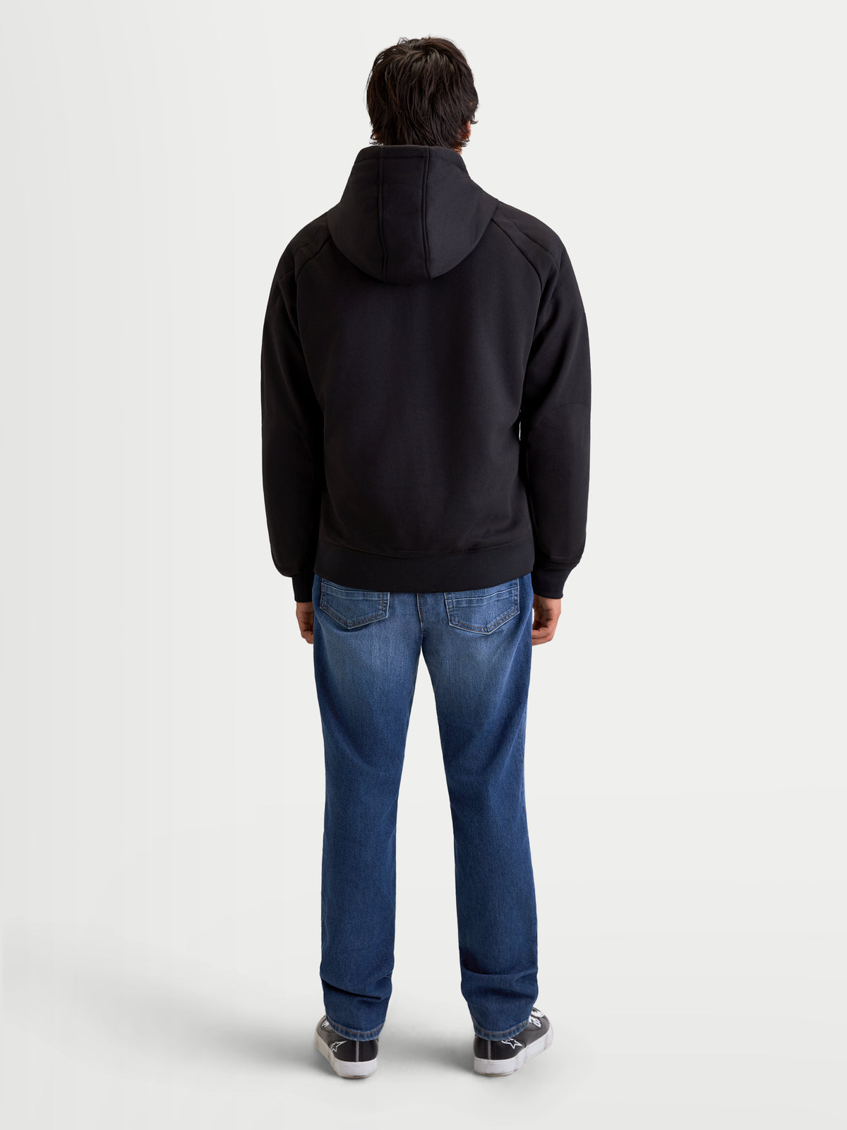 Alpinestars Ageless Hoodie, heren-motorhoodie voor stedelijk rijden in zwart, achteraanzicht op model met jeans en casual motorlaarzen, met vaste capuchon en beschermende textielconstructie