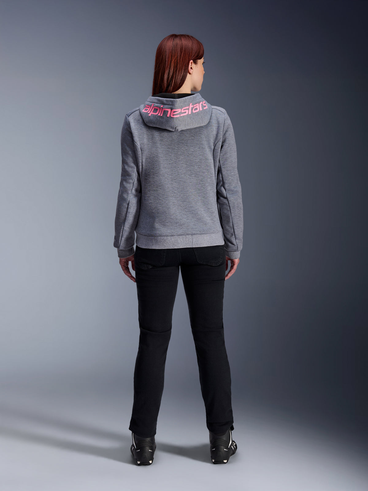 Alpinestars Stella Chrome V2 Sport Hoodie, motorhoodie voor dames, Gray Heather en Pink Fluo, achteraanzicht met roze Alpinestars-logo op de capuchon, gedragen met een zwarte motorbroek en laarzen, casual motorkleding voor dames