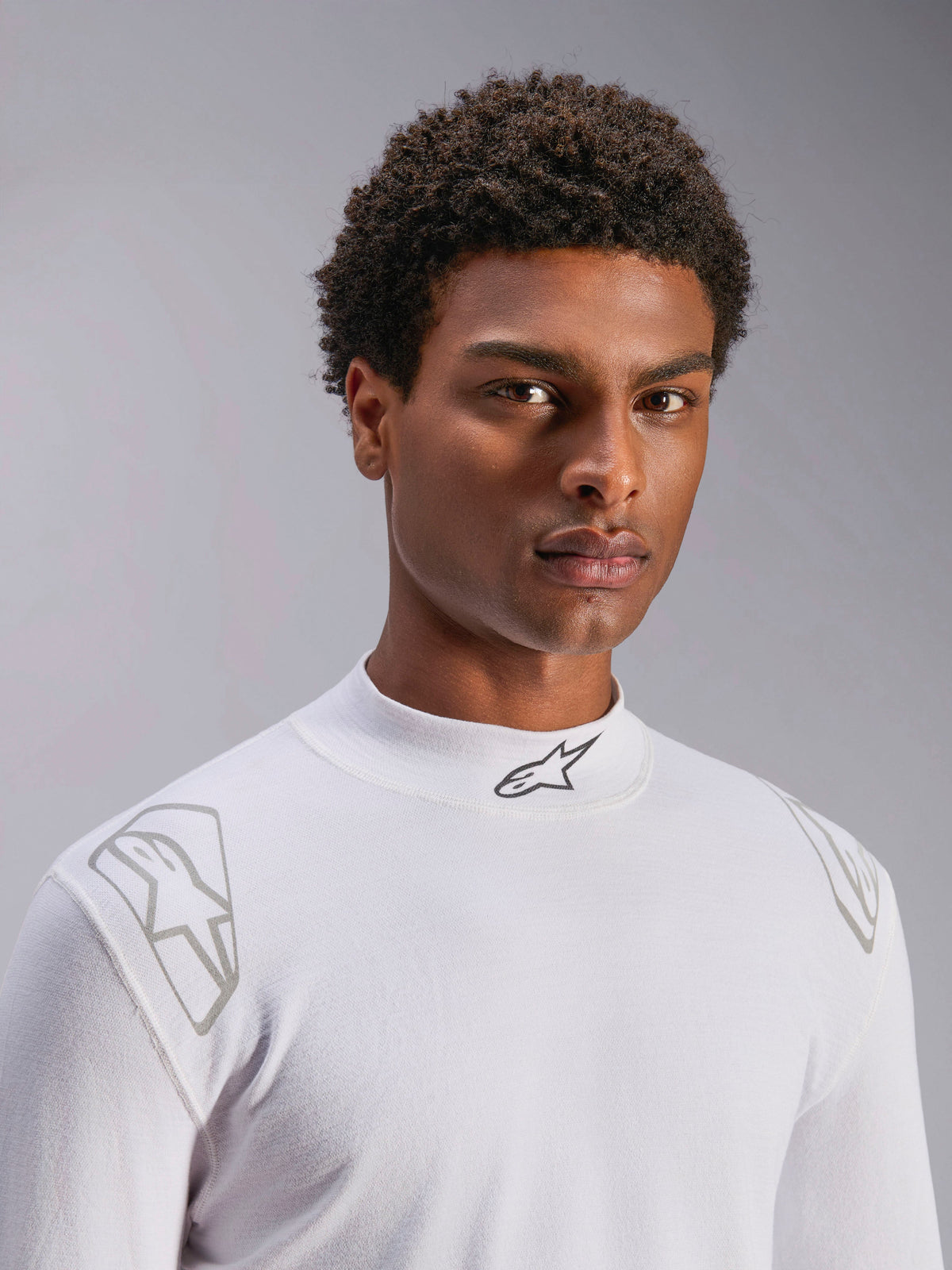 Alpinestars ZX Evo V3 Top - Lange mouwen, witte autorace baselayer, gedragen door een mannelijk model, opstaande kraag met zwart Alpinestars-logo, zilveren grafische prints op de schouders, lichtgewicht vlamvertragend autosportondergoed