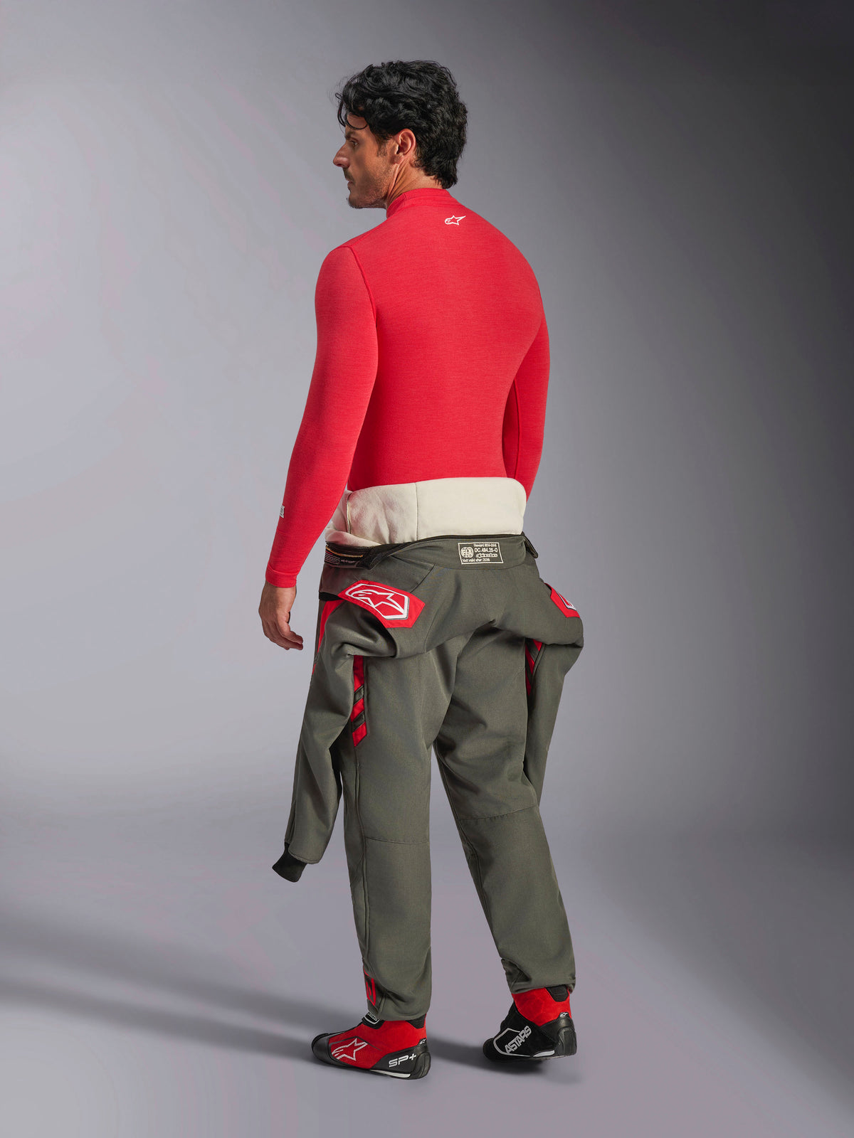 Alpinestars ZX Evo V3 Top met lange mouwen, rode auto base layer, achteraanzicht op mannelijk model met olijfgroene racepakbroek om de taille en rode raceschoenen, vlamvertragend performance ondergoed voor de autosport