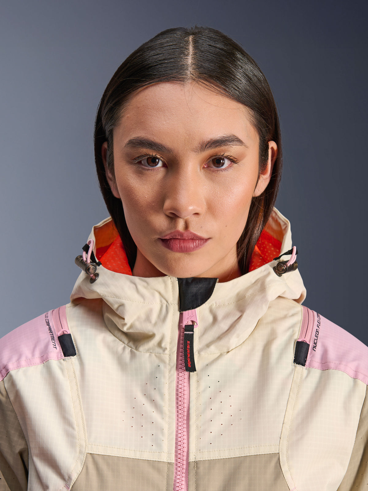 Close-up van een vrouwelijk model dat de Alpinestars Molly Air Jacket in Sand Pink Almond draagt, met een hoge kraag en capuchon met feloranje voering, roze rits aan de voorkant, ripstop-stof met lasergeperforeerde borst voor ventilatie, stedelijke motorbeschermende kleding