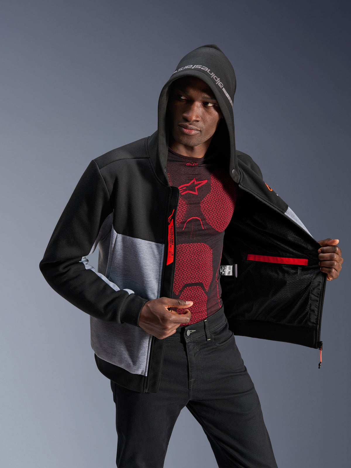 Alpinestars Chrome V2 Sport Hoodie, urban motorjas voor heren in zwart en grijs gemêleerd met rode accenten, gedragen door een model met de capuchon op, voorzien van Nucleon Flex Plus bescherming.