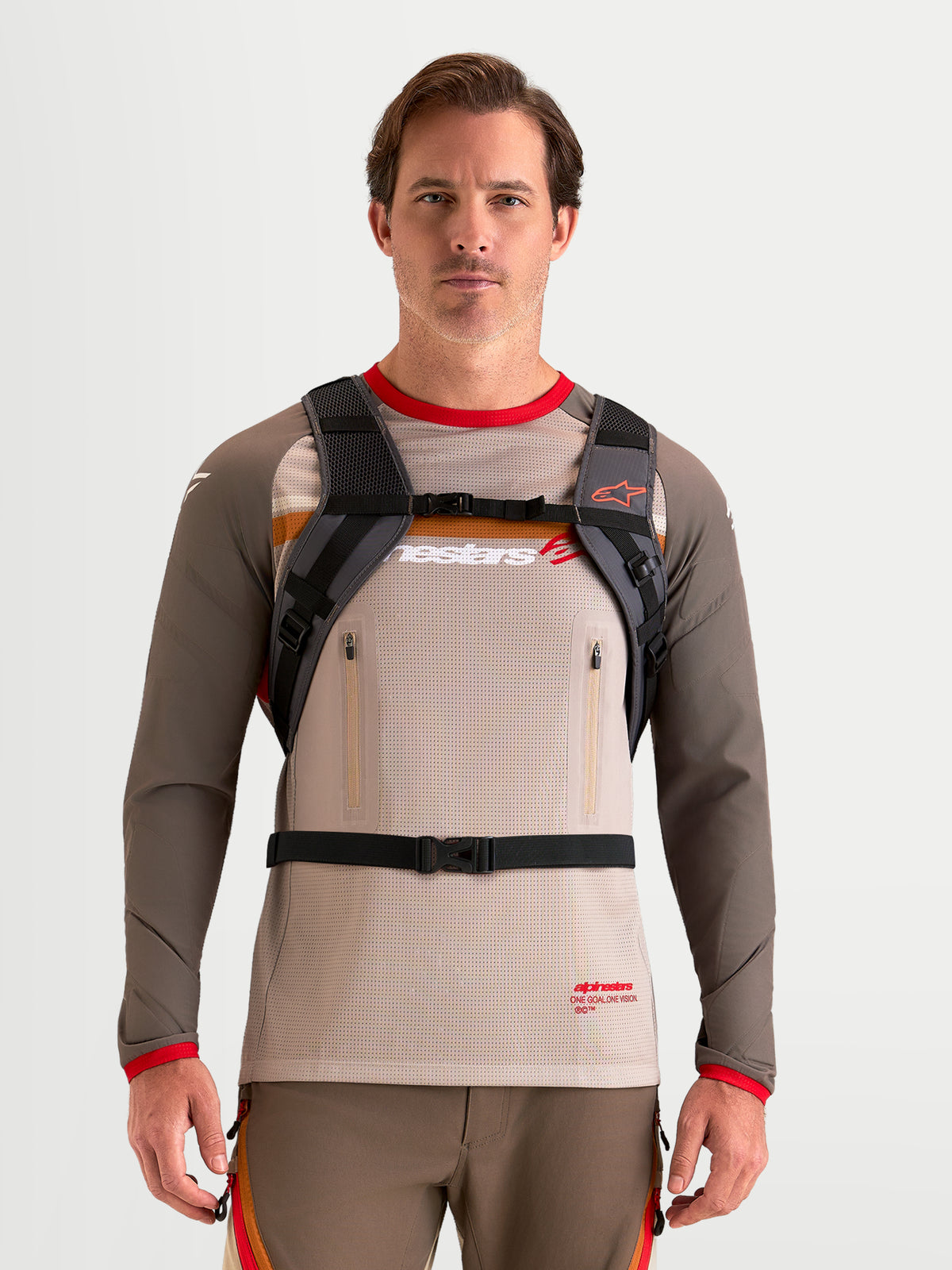 Alpinestars AT-9 rugzak, motocross rugzak in bruin en donkergrijs, vooraanzicht op model met gewatteerd schouderharnas en systeem met gespbanden