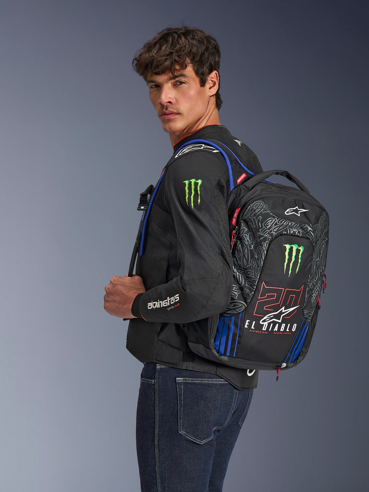 Alpinestars FQ20 City Hunter V2 Monster Backpack, Motorcycle Backpack, Black with Red Fluo, Blue, and Green, featuring Monster Energy and Fabio Quartararo 'El Diablo' branding, worn by a model with a black motorcycle jacket and jeans, streamlined design for urban riders