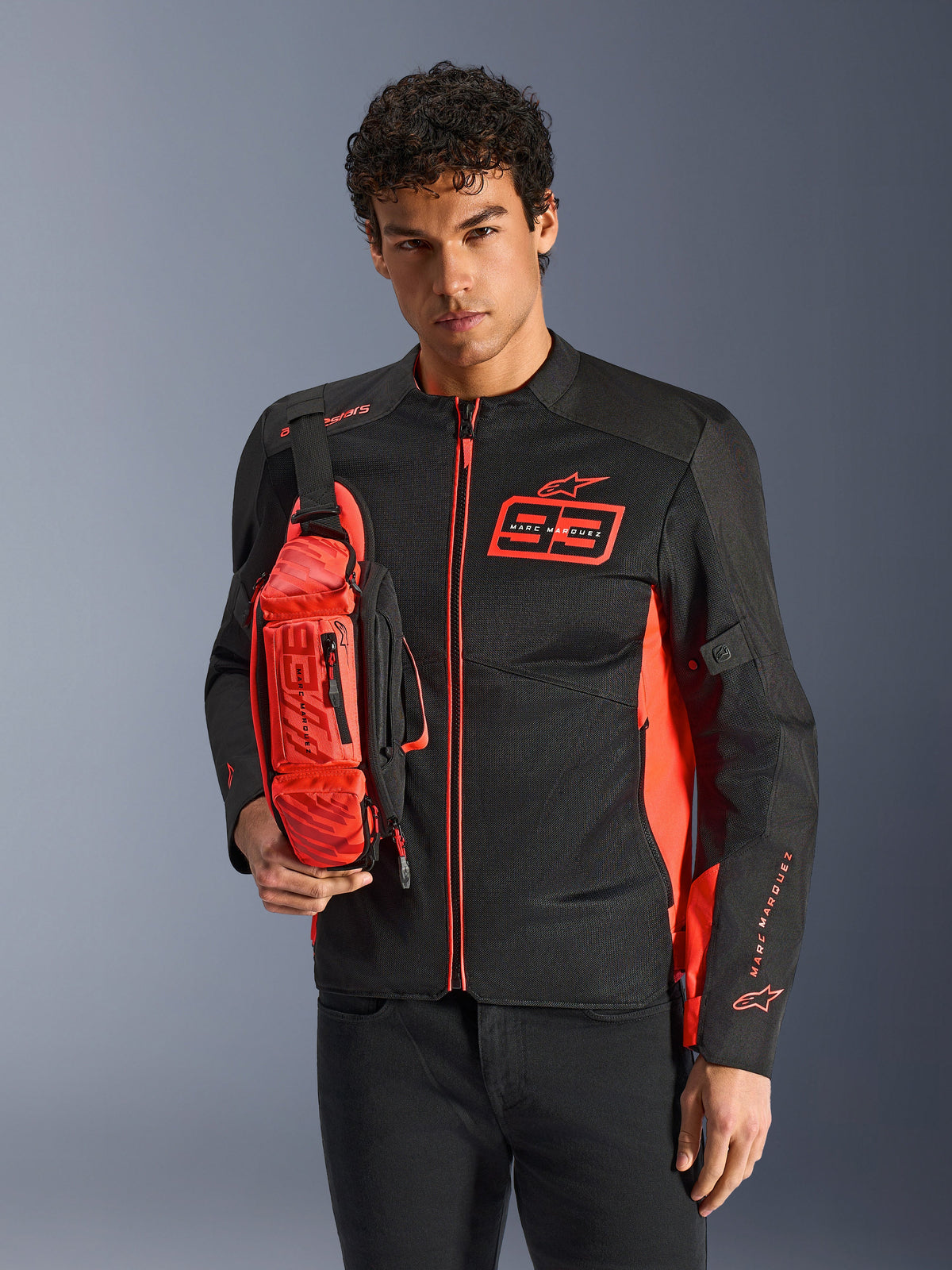 Alpinestars MM93 Waist Bag, heuptas gedragen als crossbodytas, fluo rood en zwart, man draagt bijpassend zwart en rood motorjack, voorzien van Marc Marquez 93-logo, sportief race-ontwerp