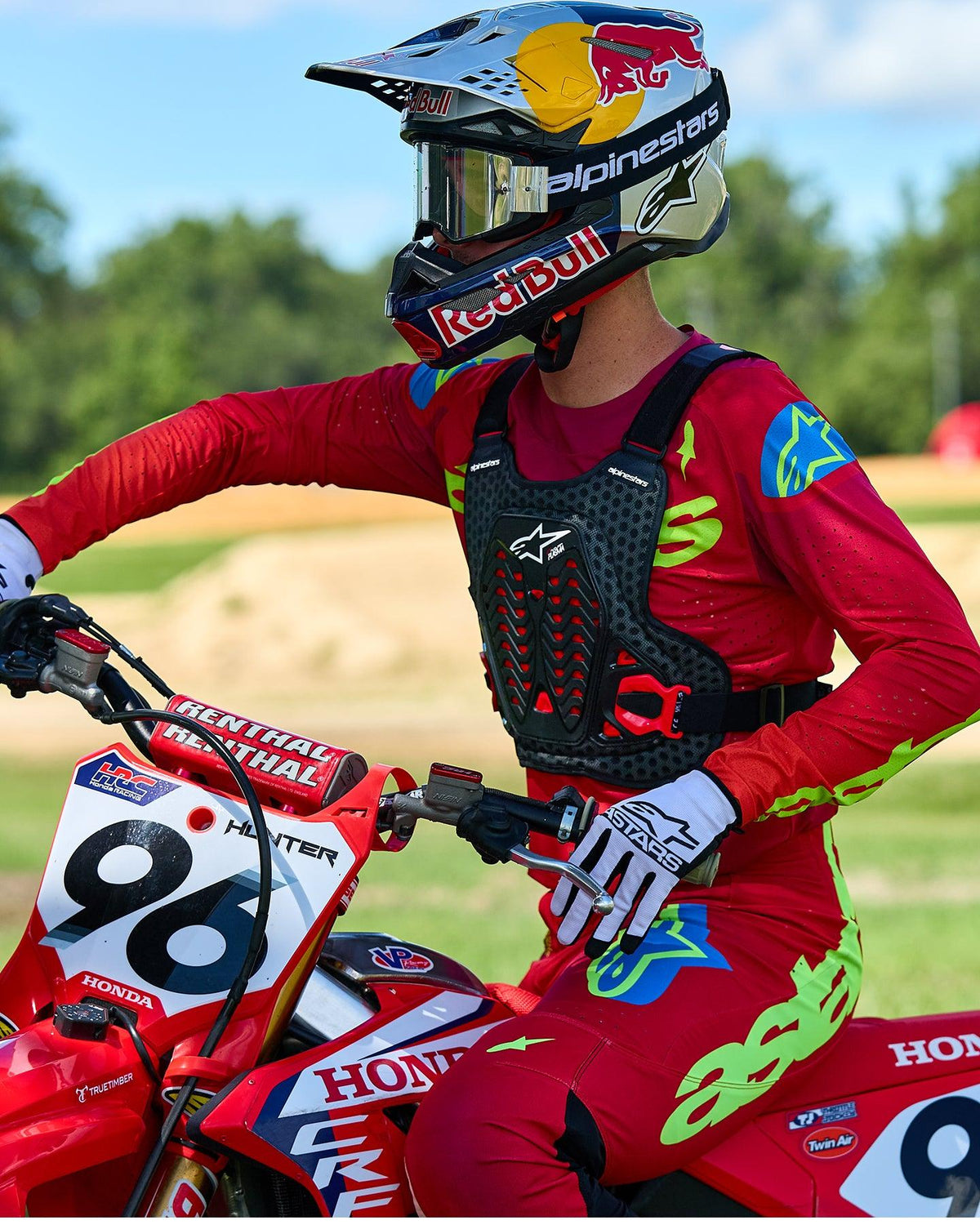 Motorcrossrijder met Alpinestars A-5 Plasma borstbeschermer in zwart en rood, gecombineerd met een rood en limegroen racejersey en broek, zittend op een rode Honda motorfiets, hoogwaardige off-road beschermende uitrusting