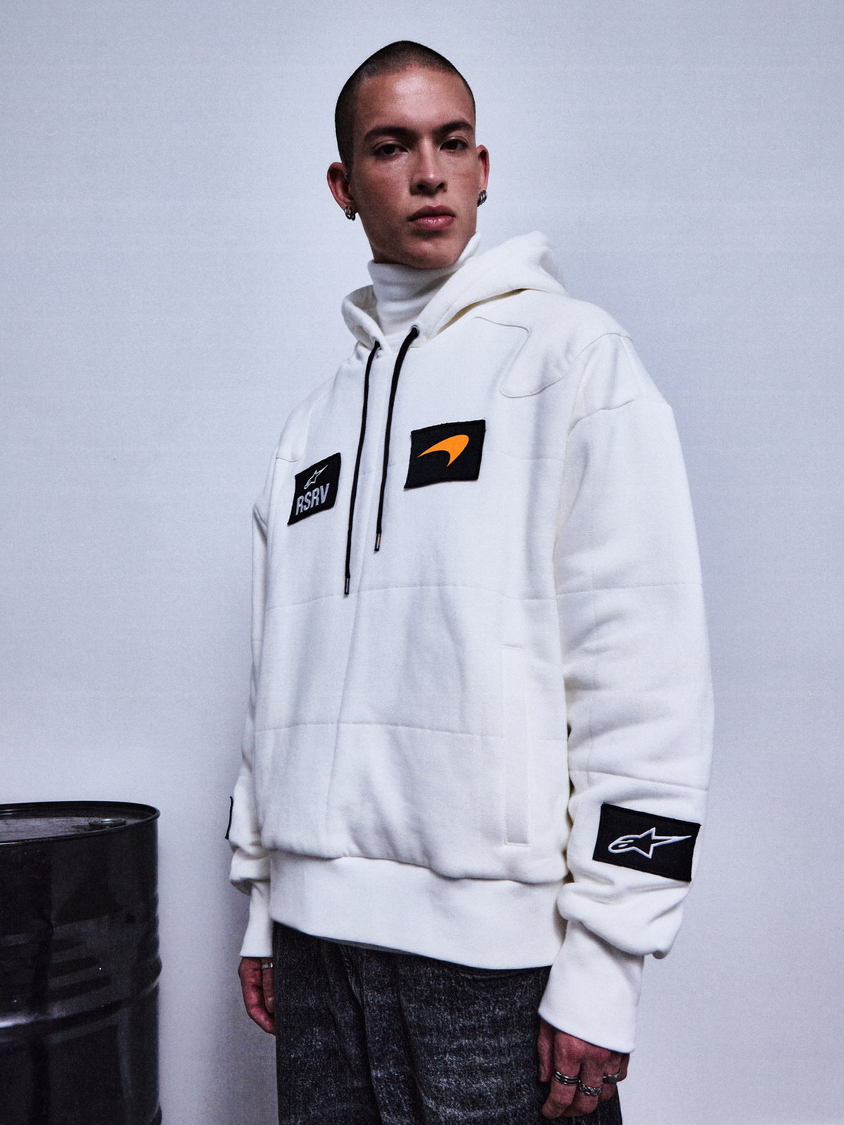 Alpinestars RSRV Rival hoodie, premium streetwear hoodie, wit met zwarte patches, oranje swoosh detail, RSRV logo, unisex lifestyle collectie, gedragen met grijze broek