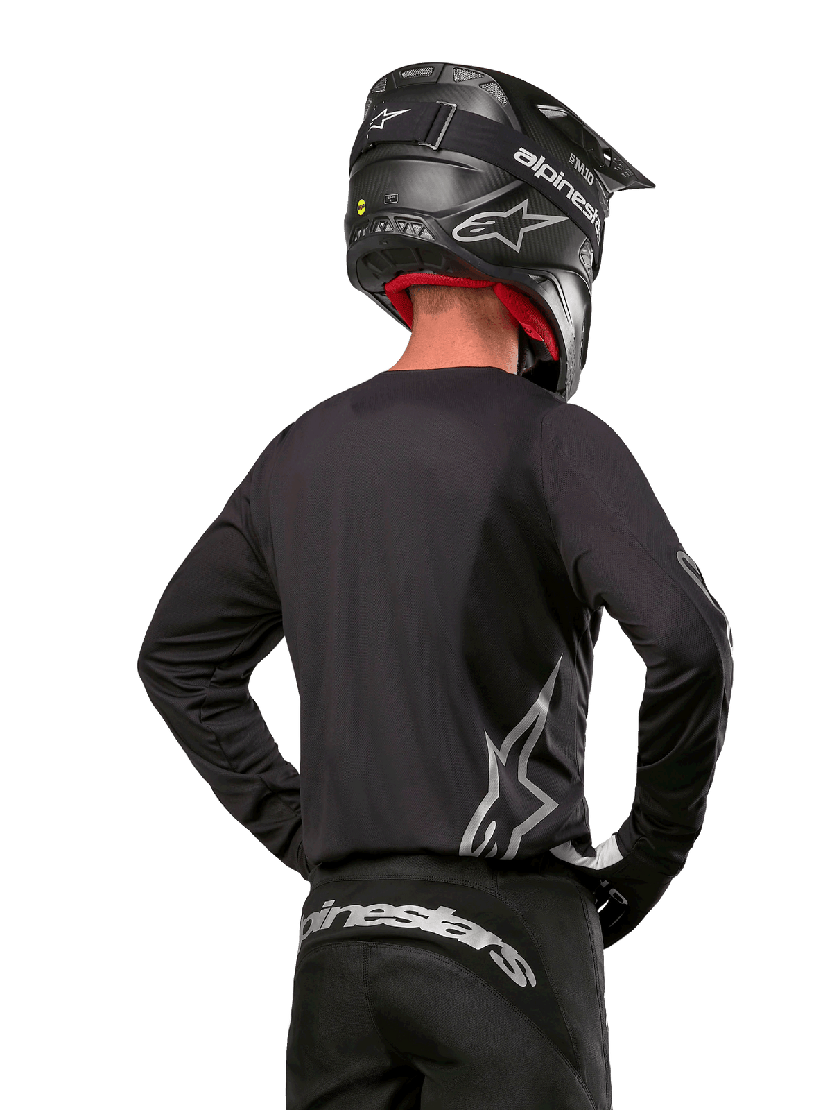 Alpinestars 2024 Fluid Graphite Gear Set, motorcross shirt en broek, grafiet en zilver, achteraanzicht met zilveren logo's op de onderrug en taille, gedragen met zwarte helm met carbon-effect, lichtgewicht poly-stof ontwerp voor off-road rijden