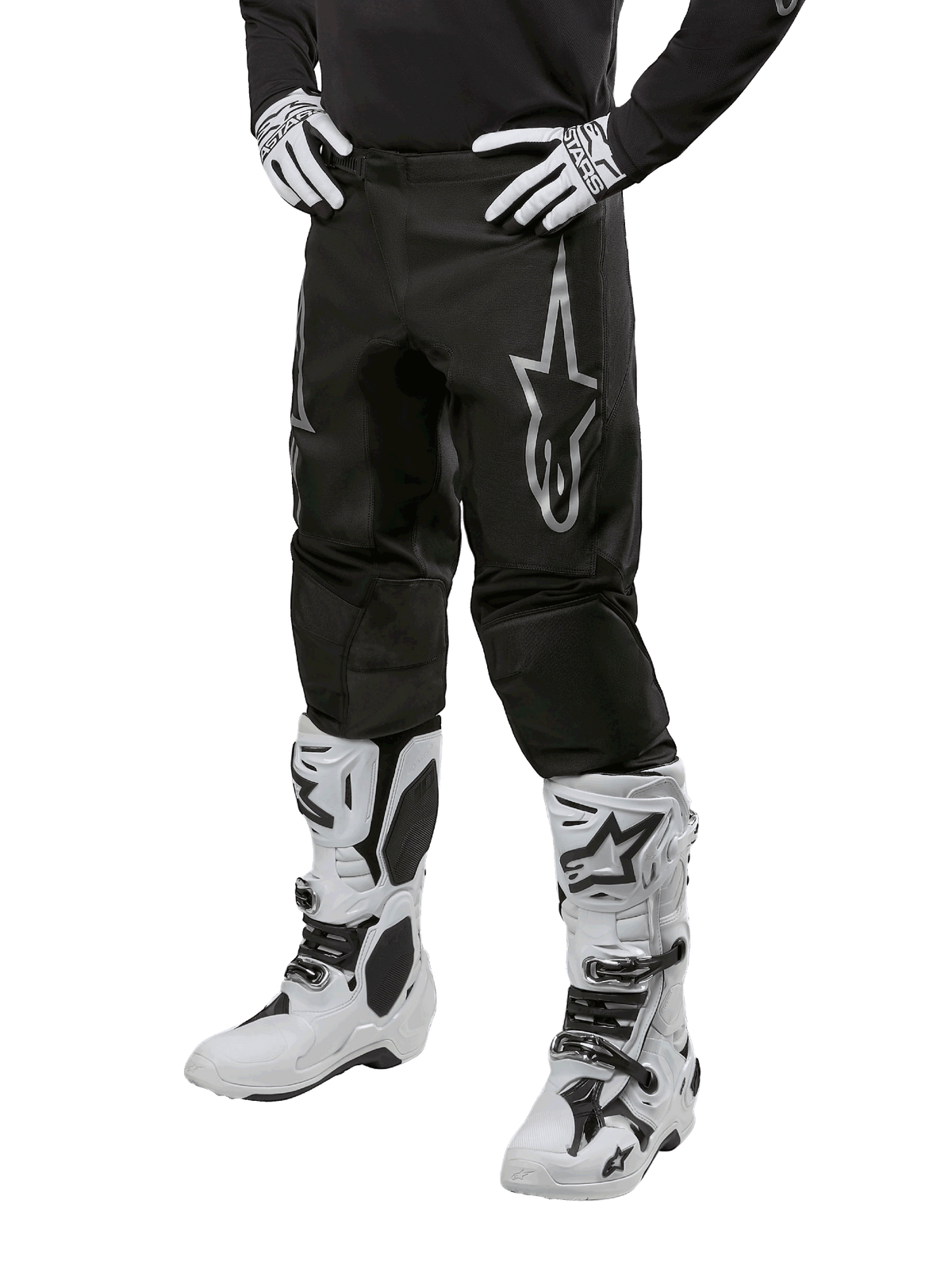 Alpinestars 2024 Fluid Graphite crossbroek, motorcross broek, grijs en zwart, gedragen met witte en zwarte motorcrosslaarzen en handschoenen, met een groot zilveren Alpinestars-logo op het bovenbeen, sportieve pasvorm voor off-road rijden